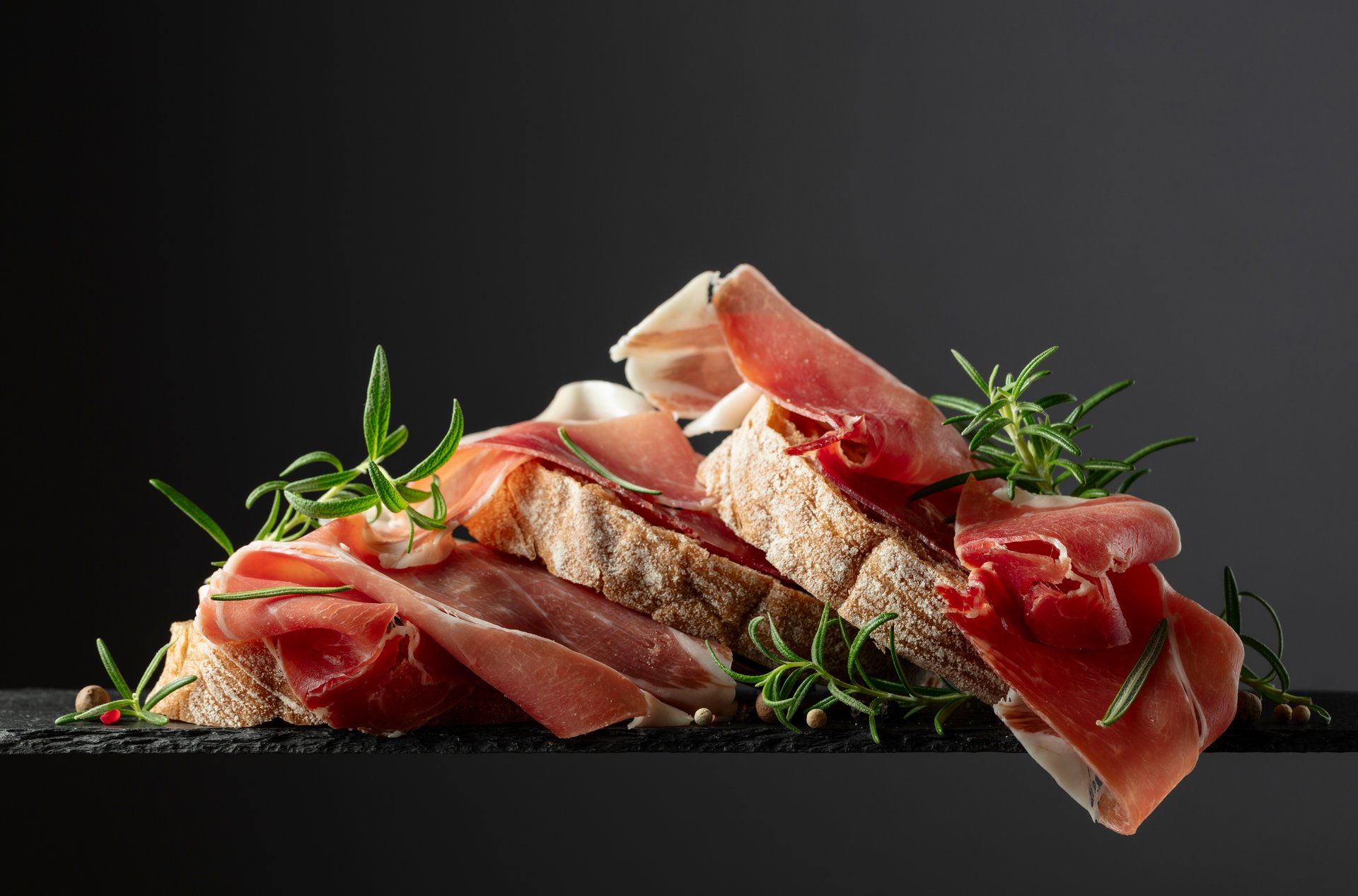 Ciabatta with prosciutto and rosemary on a black background. Traditional Italian snack.