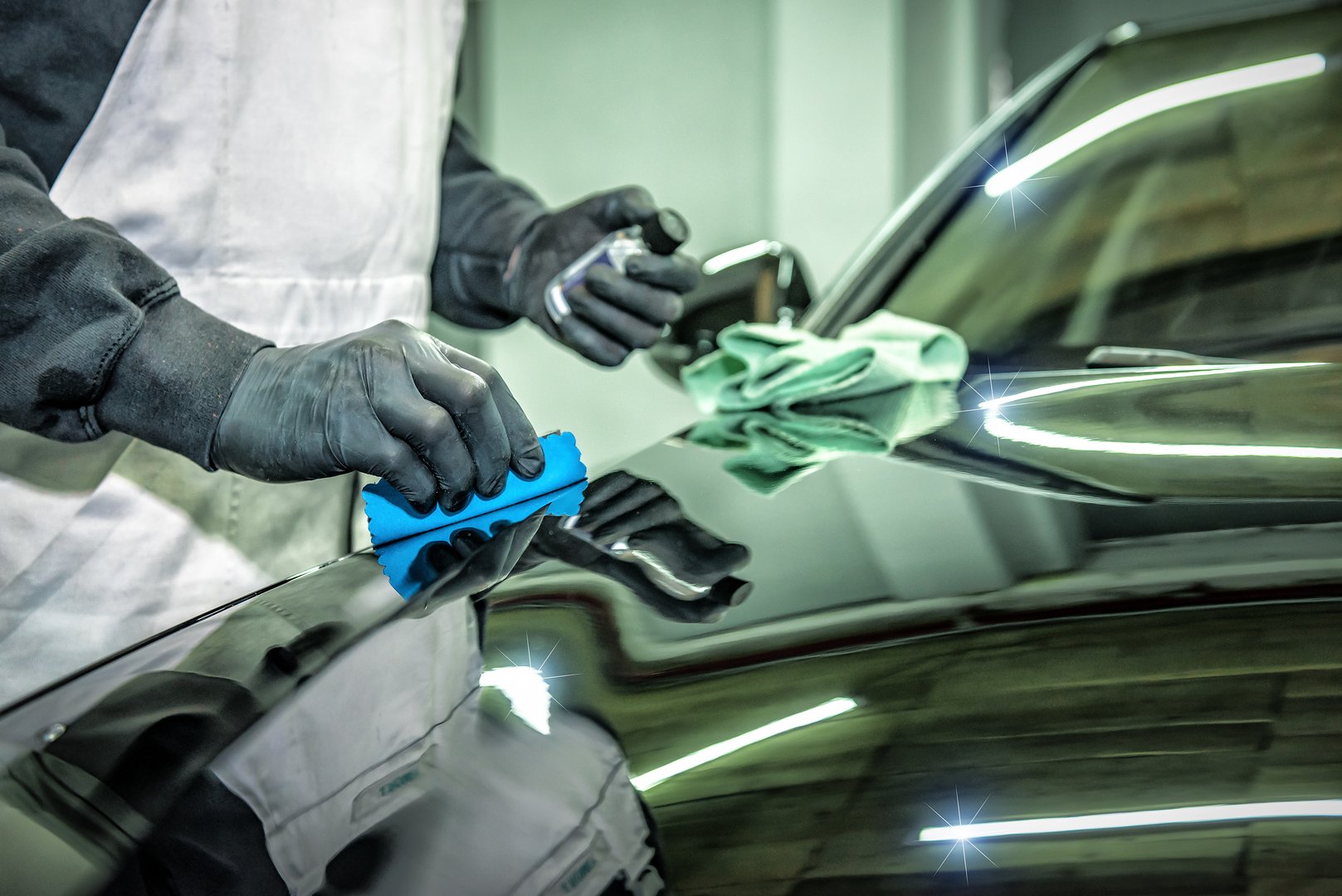 Car detailing or car wash worker applying ceramic nano coating on black car hood. Industrial theme