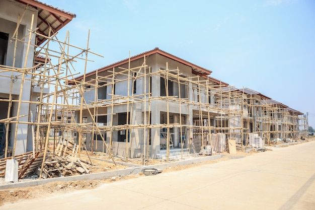 Row of unfinished houses with bamboo scaffolding at a construction site under a clear blue sky.