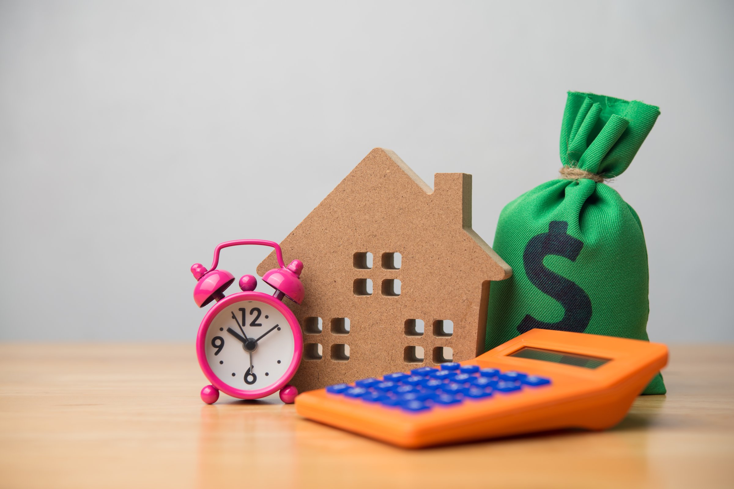 House, alarm clock, money bag and calculator on table white wall background. Home finance, expenses, spending money, financial planning, mortgage loan, homebuyer, due date debt repayment concept.