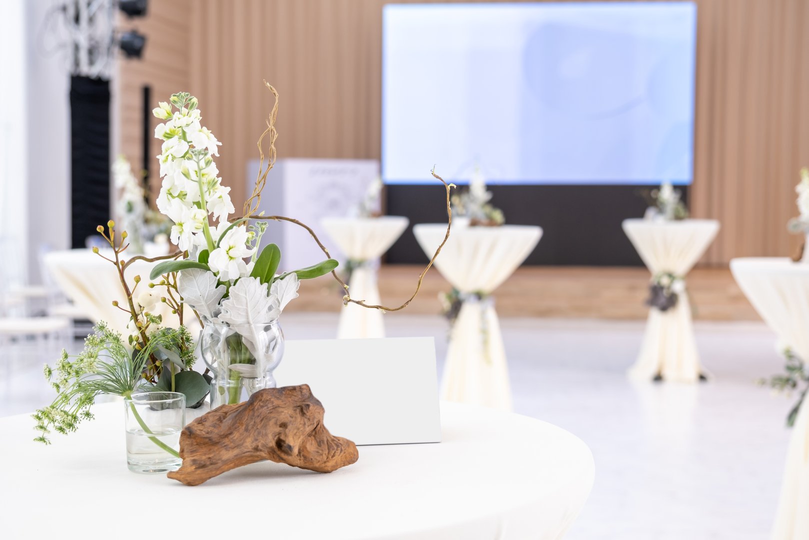 Table covered with white cloth decorated with twigs and white flowers at a wedding banquet in a hotel.