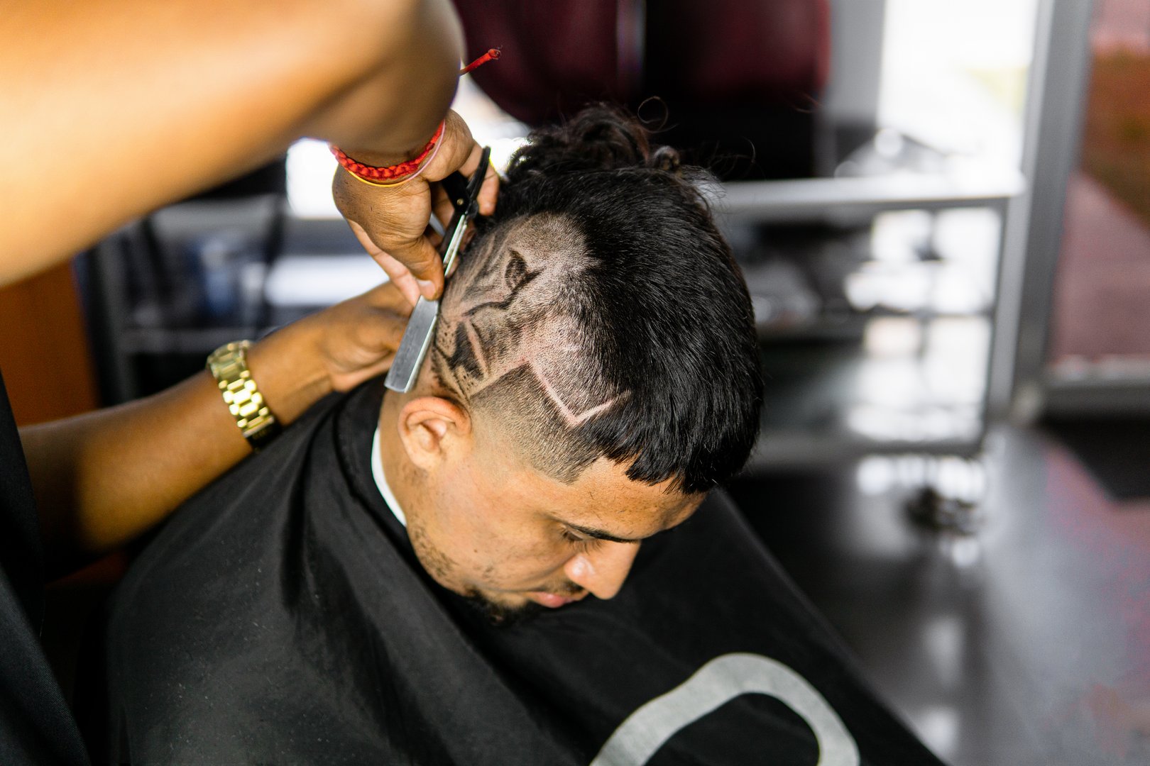 A skilled barber gives a male client a modern haircut with a creative pattern shaved into his hair at a professional barbershop.