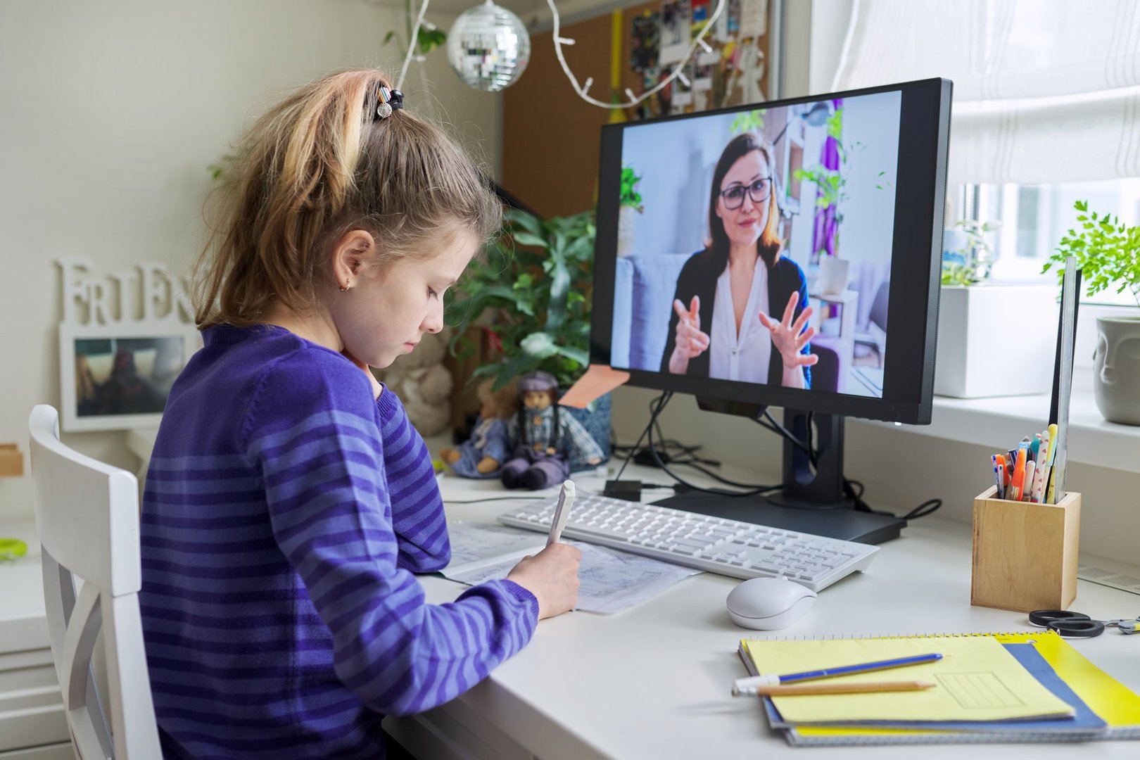 Young child girl studying with teacher remotely on computer using video call
