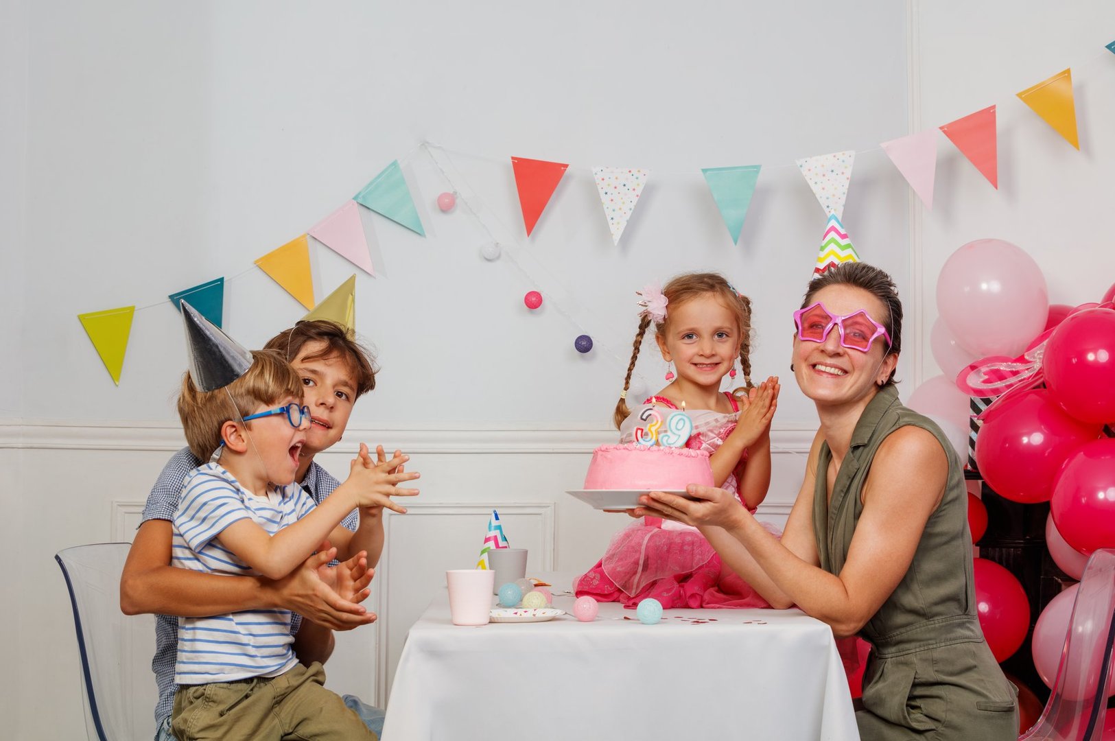Gathered at a party, the family of four, mother father two kids enthusiastically celebrates a birthday, complete with a pink cake and vibrant decorations