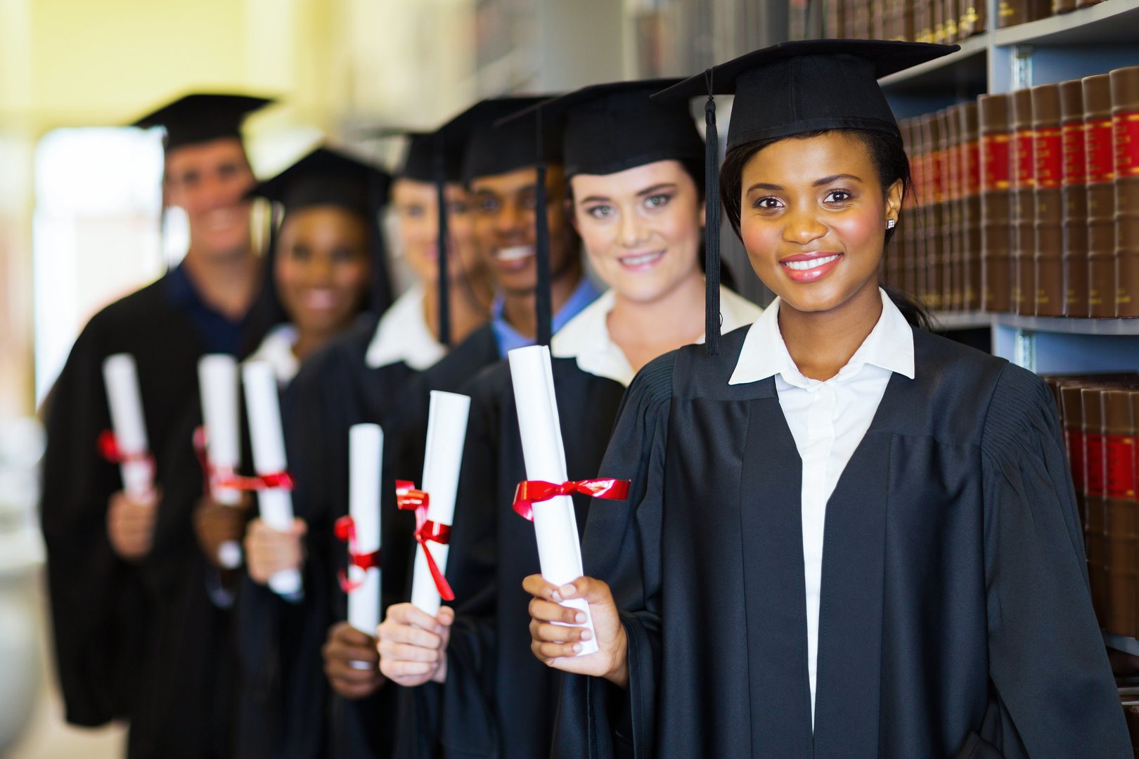 group of happy graduates holding diploma in library