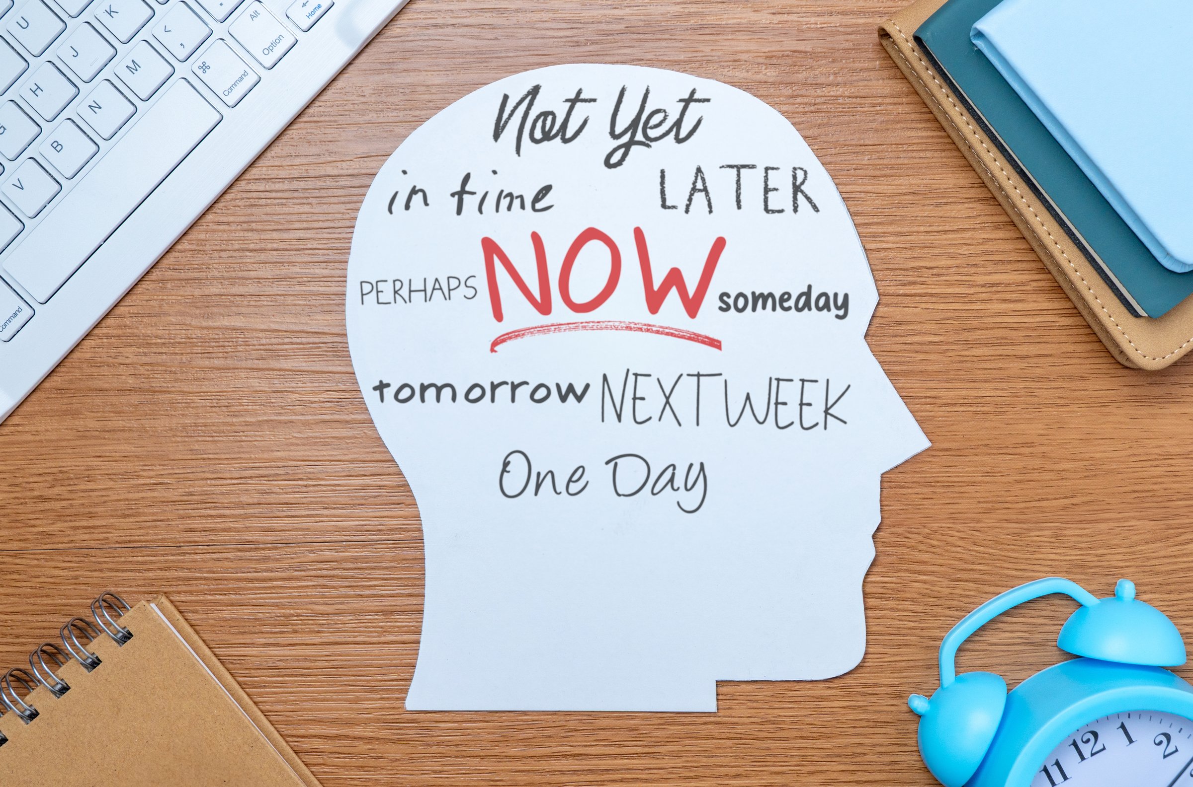 A paper cutout in the shape of a human head on a table with various words related to time and delay. Procrastination, time management concept.