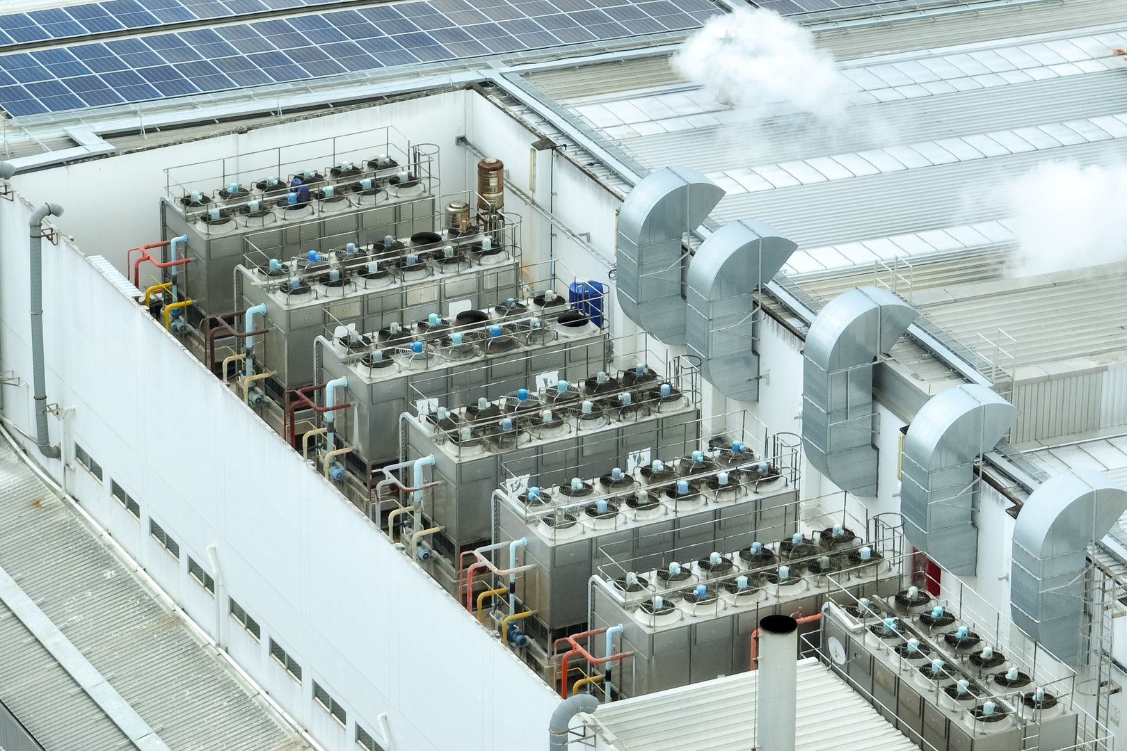 Sustainable industrial rooftop. Aerial view showcasing solar panels, ventilation systems, and industrial chillers. Renewable energy and efficient cooling in modern manufacturing facilities.