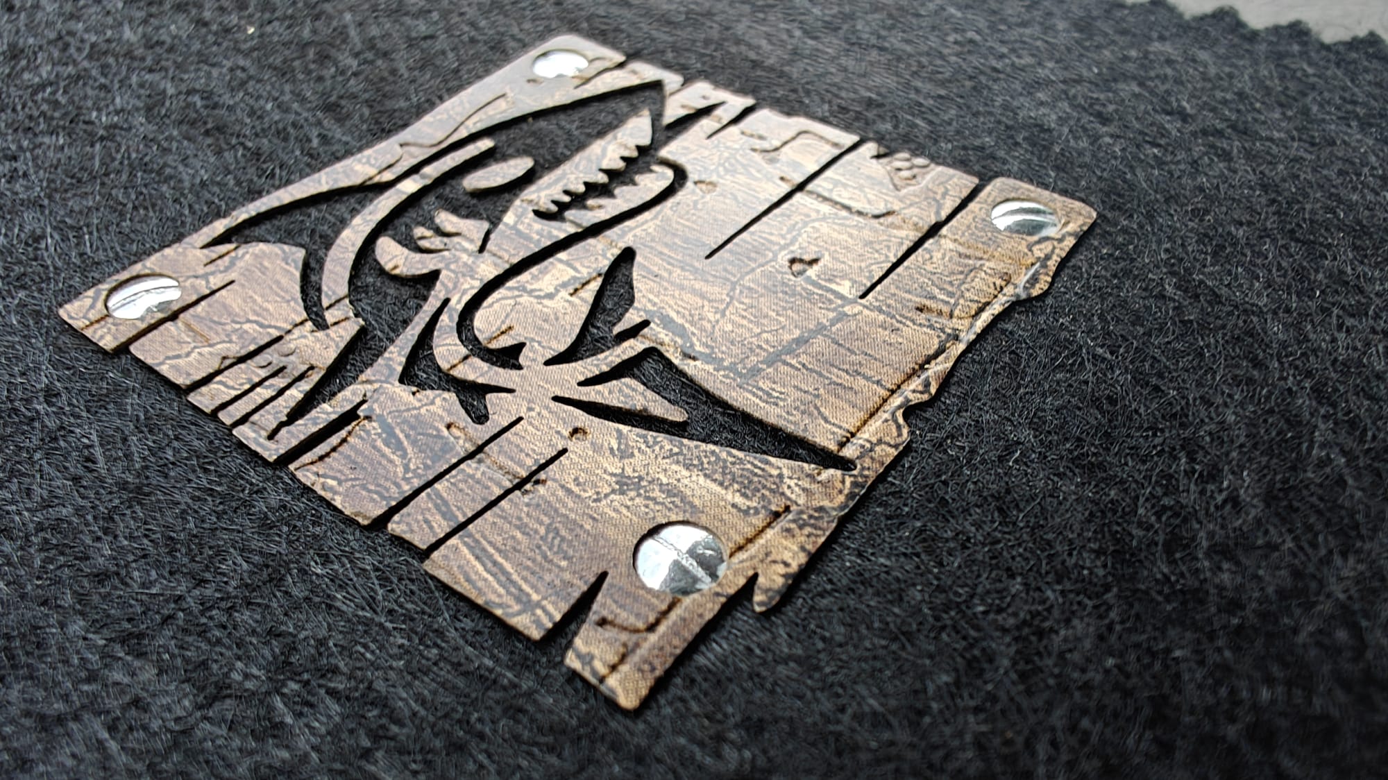 Metal shark cutout with bolts on textured black fabric.