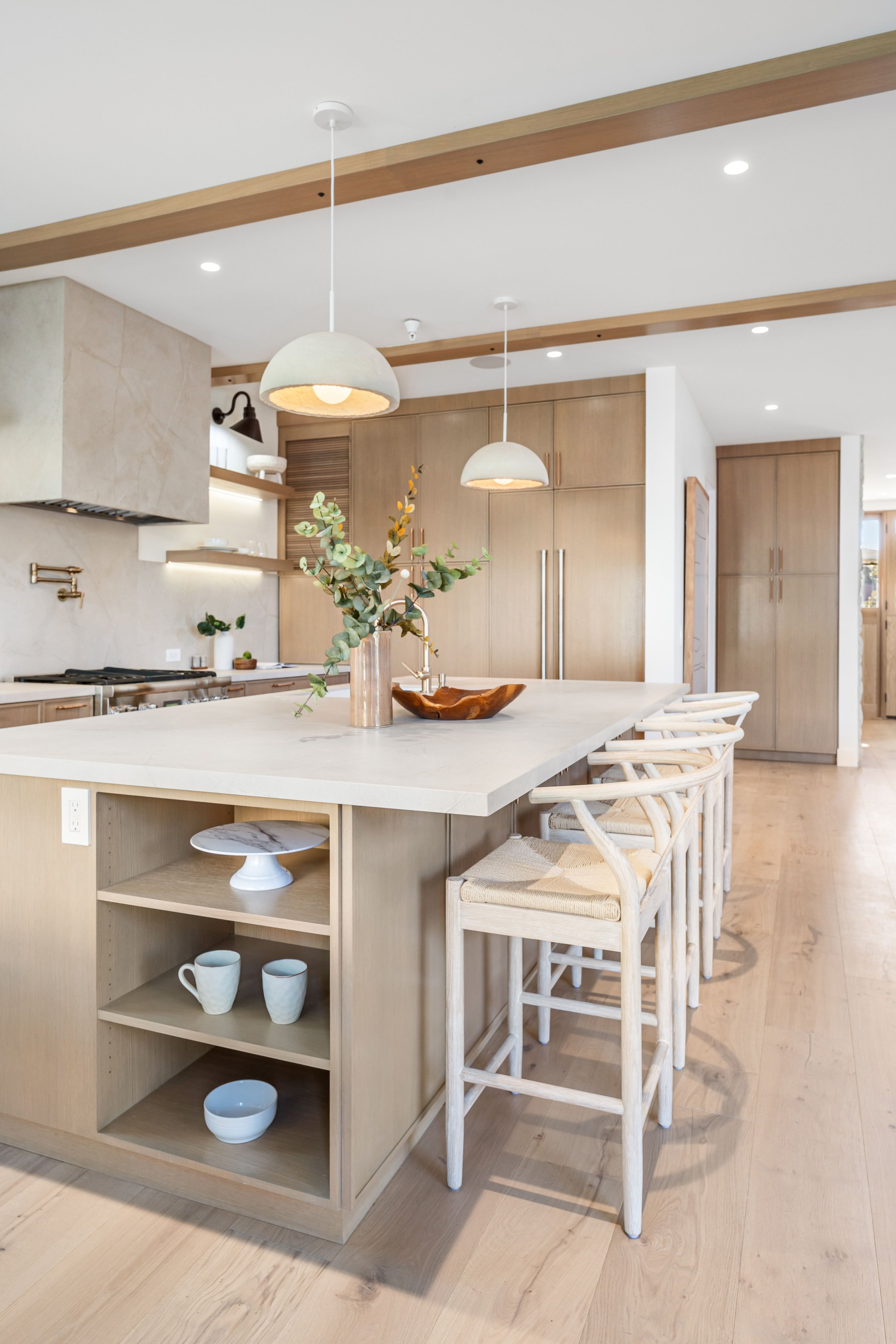 Modern kitchen interior with wooden cabinets, island, and pendant lights, featuring elegant decor and natural light.