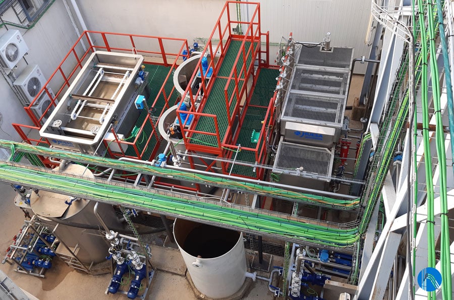 Aerial view of an industrial water treatment facility with tanks, pipes, and metal structures in a compact arrangement.