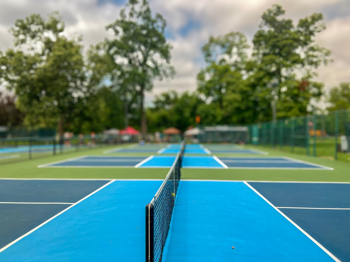 Selective focus on new paddleball courts. A small group of players are in the distance. City public park setting with cloudy blue skies.