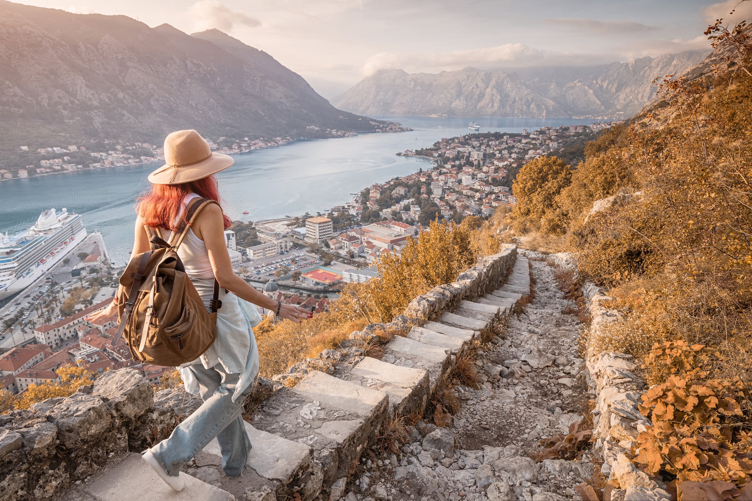 Female tourist descending ancient stone steps, savoring breathtaking view of Kotor bay at sunset in Montenegro