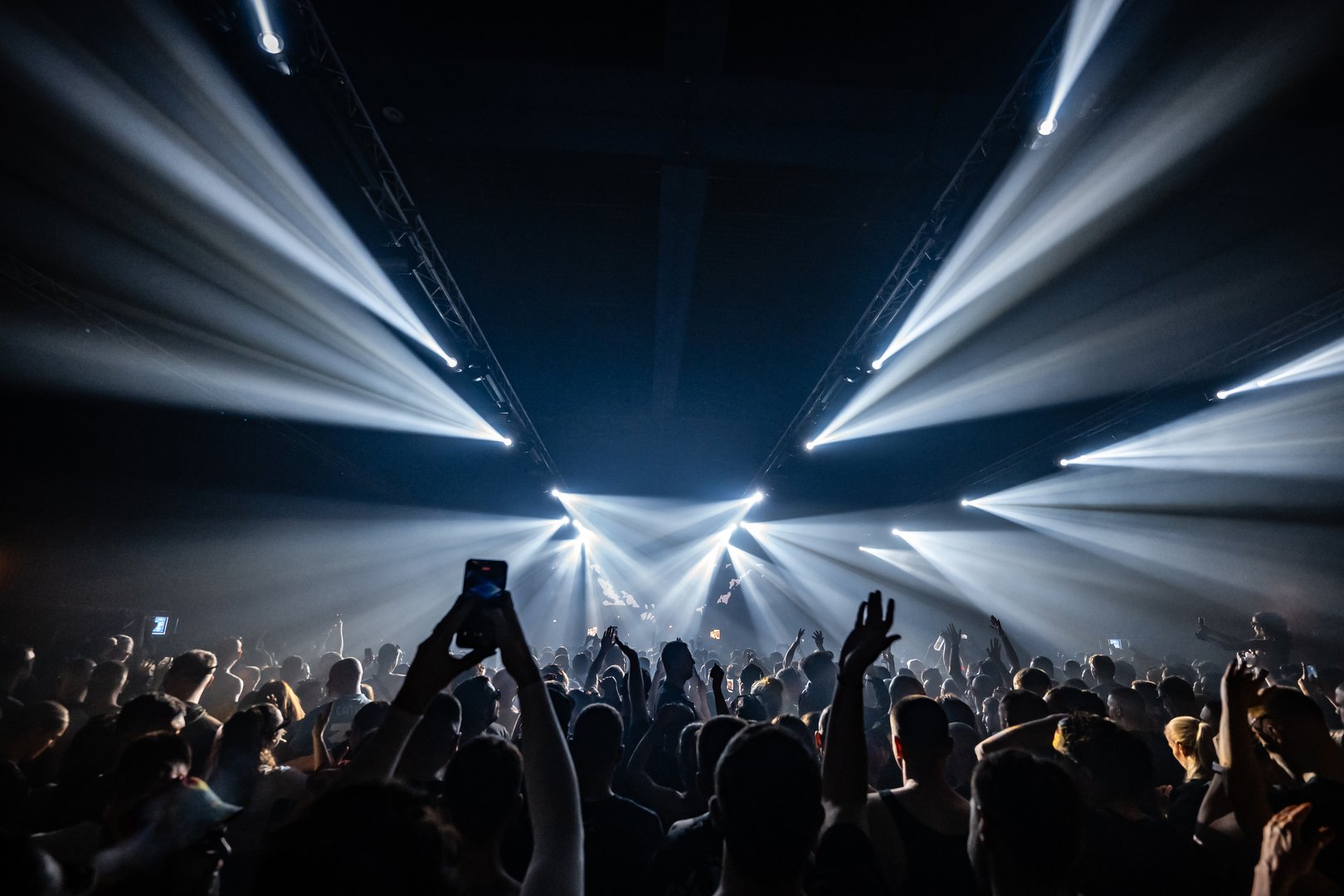 Fans recording and cheering during a vibrant live music concert, illuminated by powerful stage lights creating a captivating atmosphere