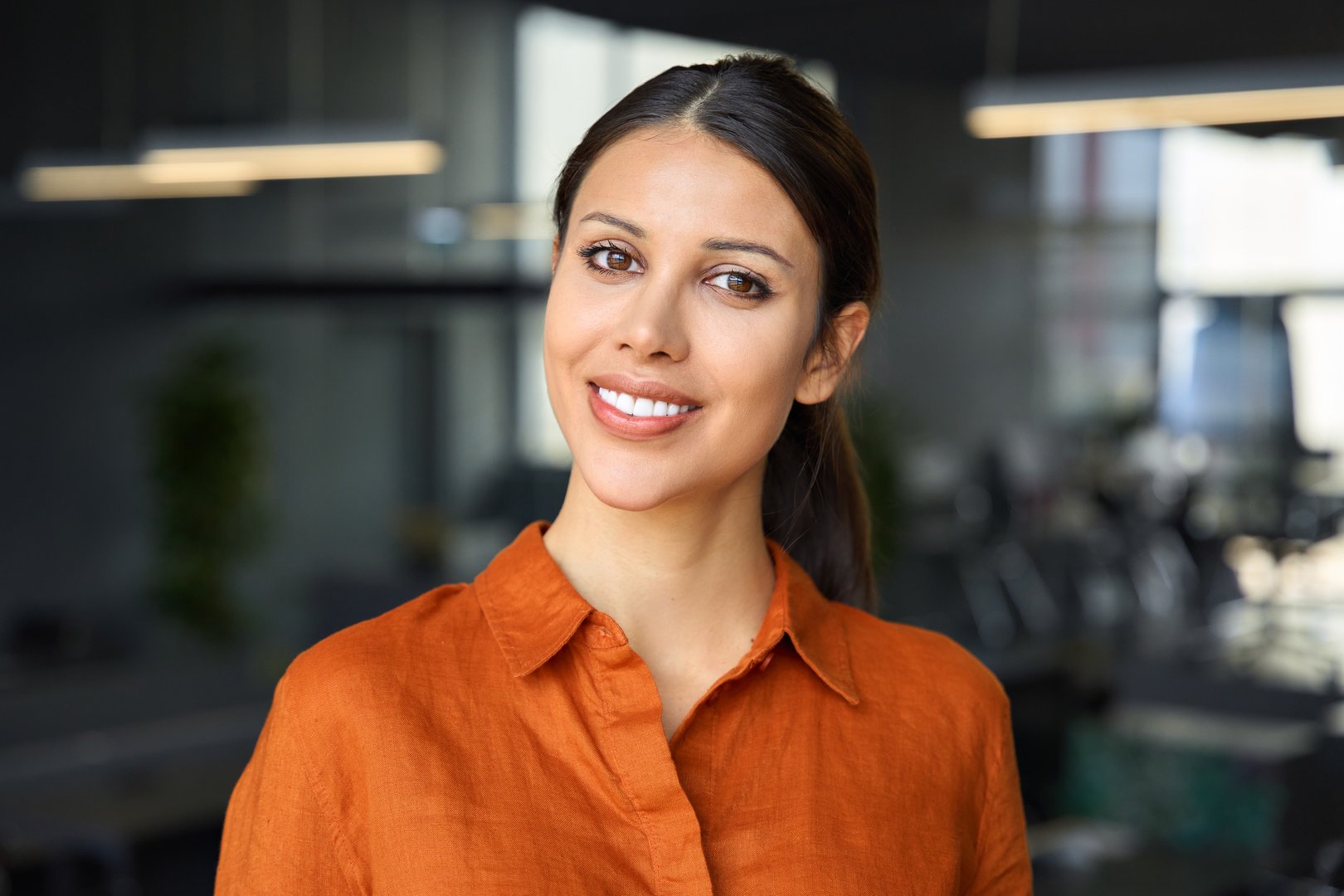 Headshot closeup portrait of beautiful successful hispanic young business woman smiling looking at camera. Latin or eastern confident middle age female ceo leader businesswoman standing in office.