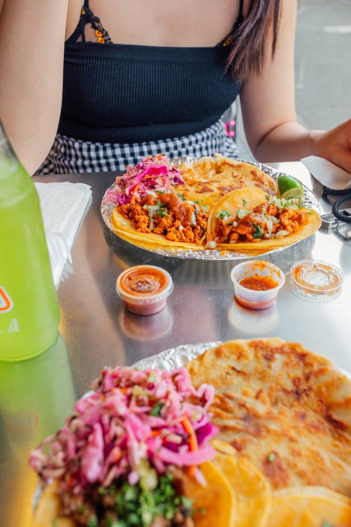 woman eating plates of tacos, pupusas at Taqueria with bottle of lime soda