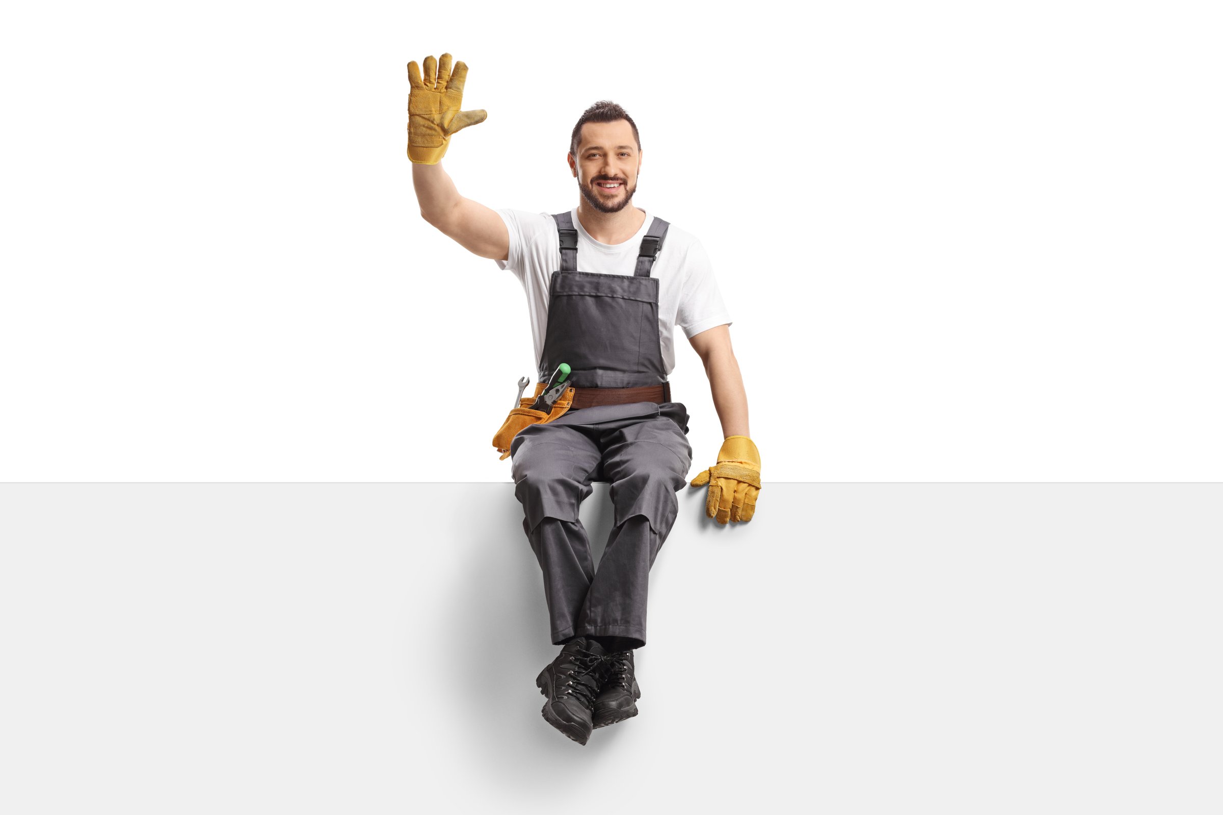 Repairman sitting on a blank panel and waving isolated on white background
