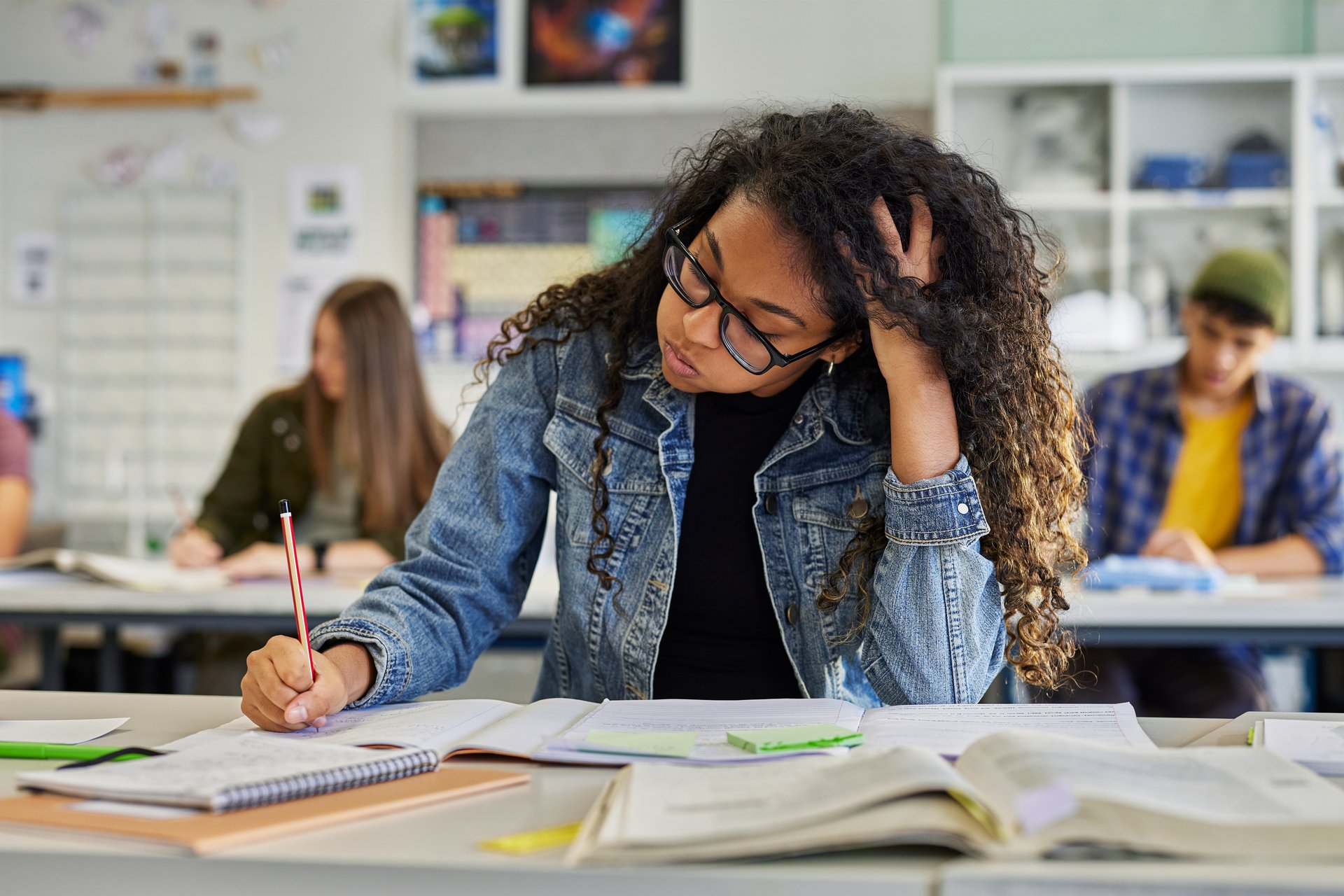 Black tired student writing in class during exam while snorting. Anxious young african american woman with hand on head feeling tired while studying at school. Troubled and stressed girl doing exam that doesn't know the answers.