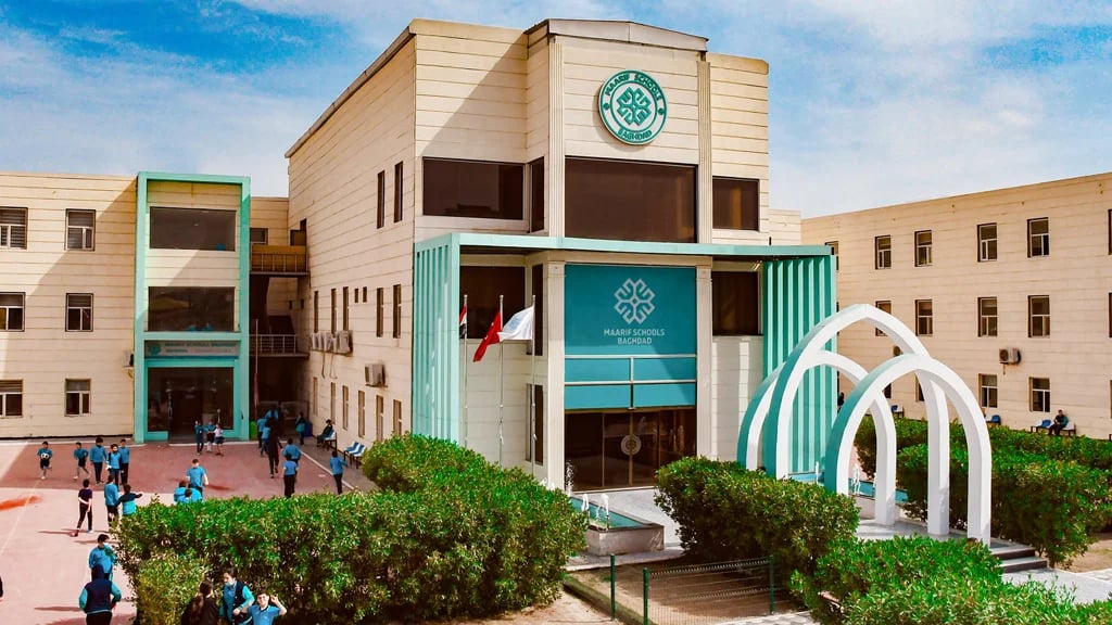 A modern school building with a distinct logo, students in uniforms outside, and two green arches near the entrance.