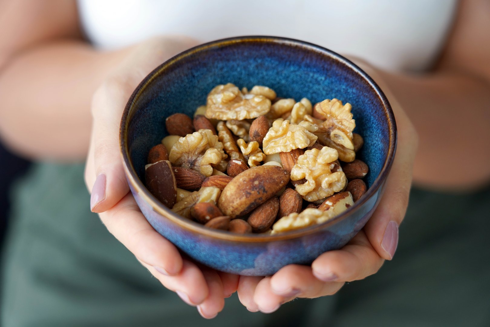 Woman hands showing a bowl full of variety of nuts mix of dried fruits