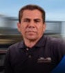 Man in a dark polo shirt with blurred background, appearing serious.