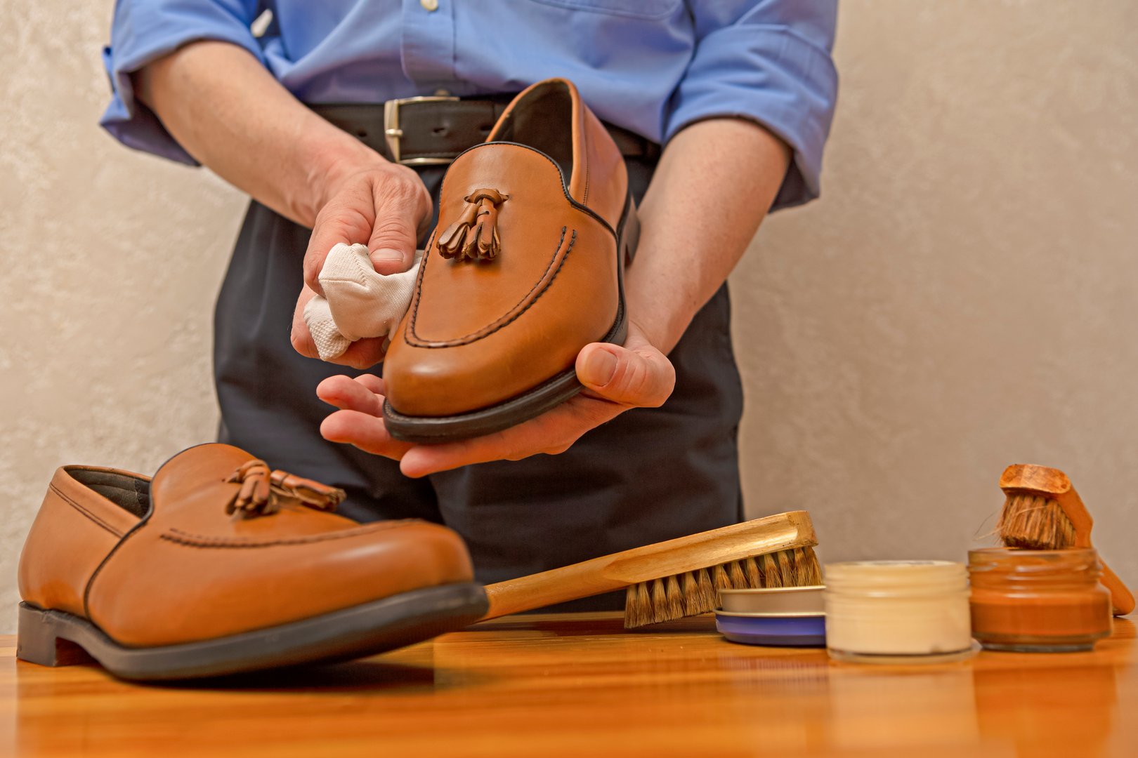 Hands of Professional Male Shoes Cleaner with Cleaning Brushes For Tan Tassel Loafers Leather Shoes While Working in Workshop With Soft Cloth. Horizontal Image Composition