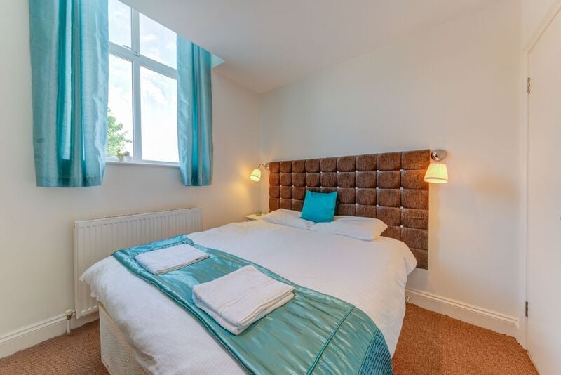 A bedroom with a large bed, blue accents, and wall-mounted lamps, featuring a tufted headboard and sheer blue curtains.