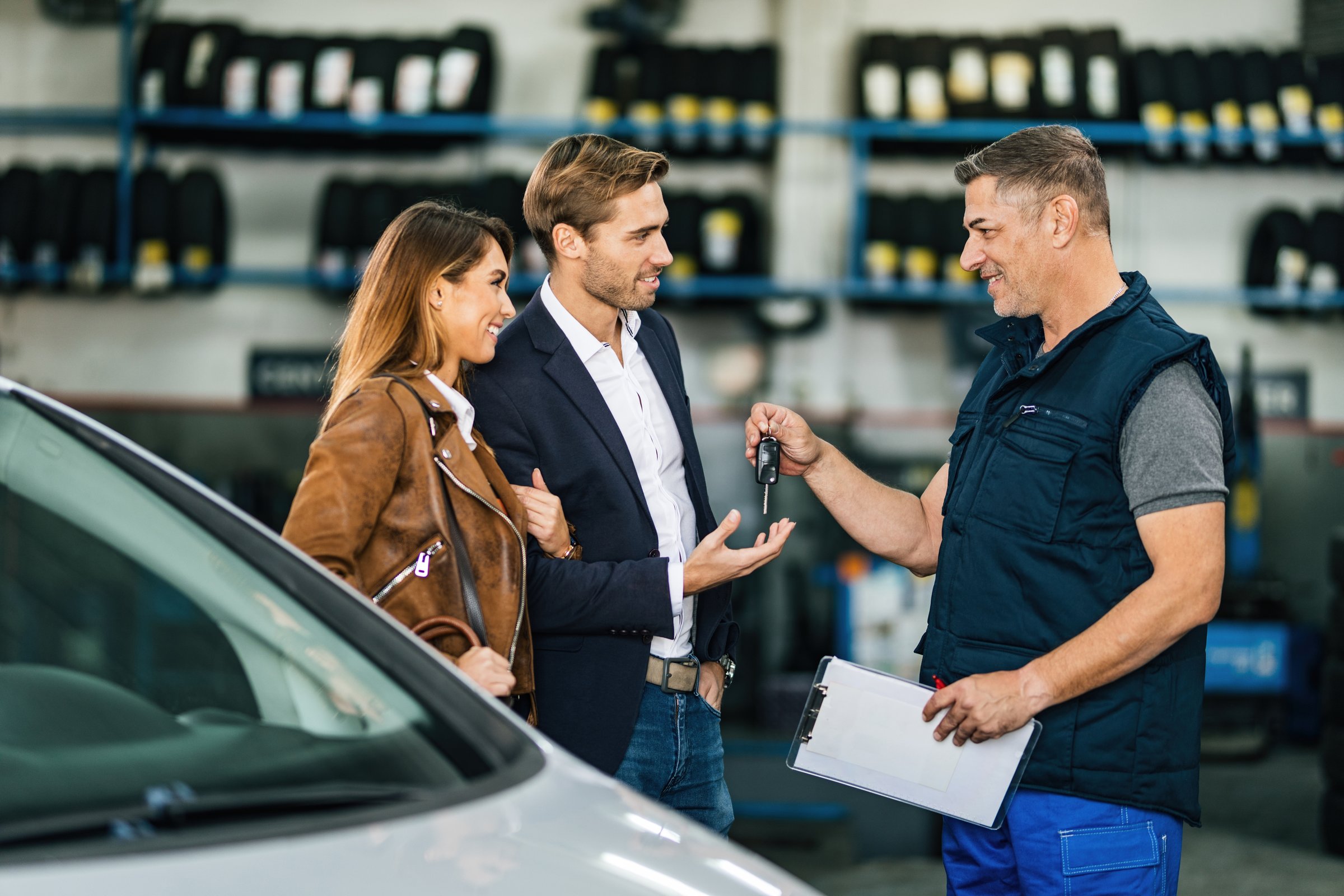 Happy mechanic giving car key to a young couple at auto repair shop