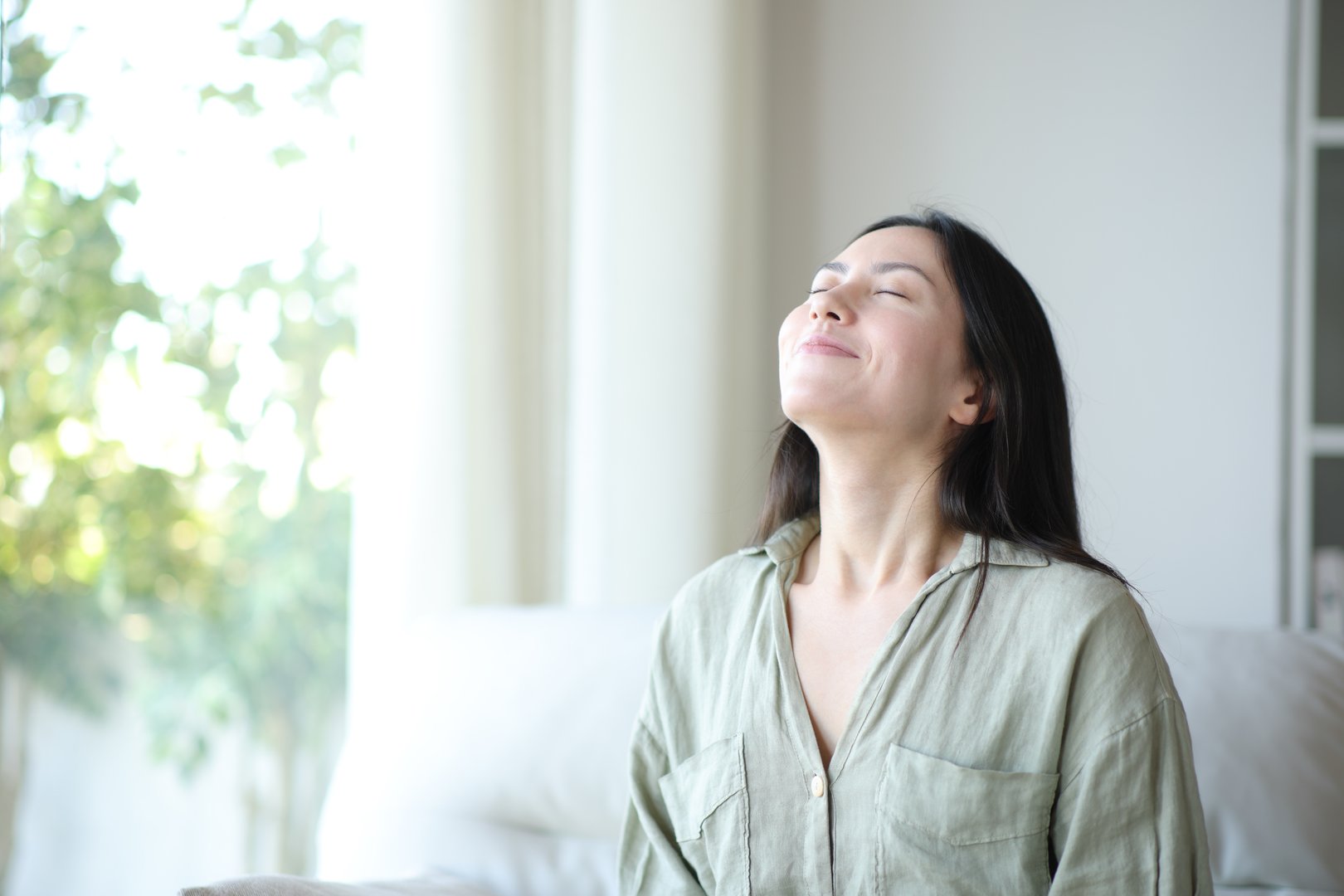 Asian woman breathing fresh air sitting on a sofa at home