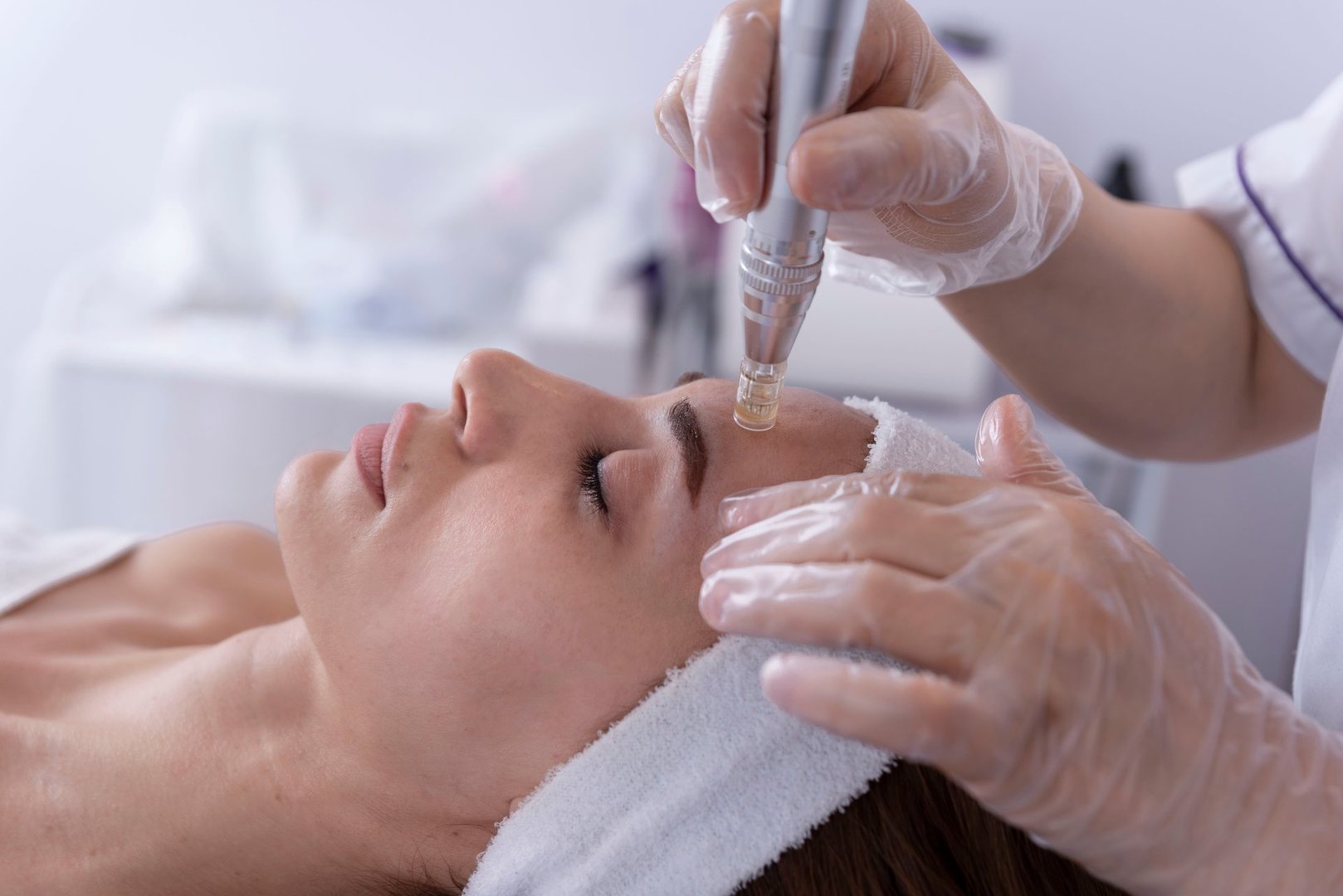 Cosmetologist applying facial dermapen treatment on face of young woman customer in beauty salon