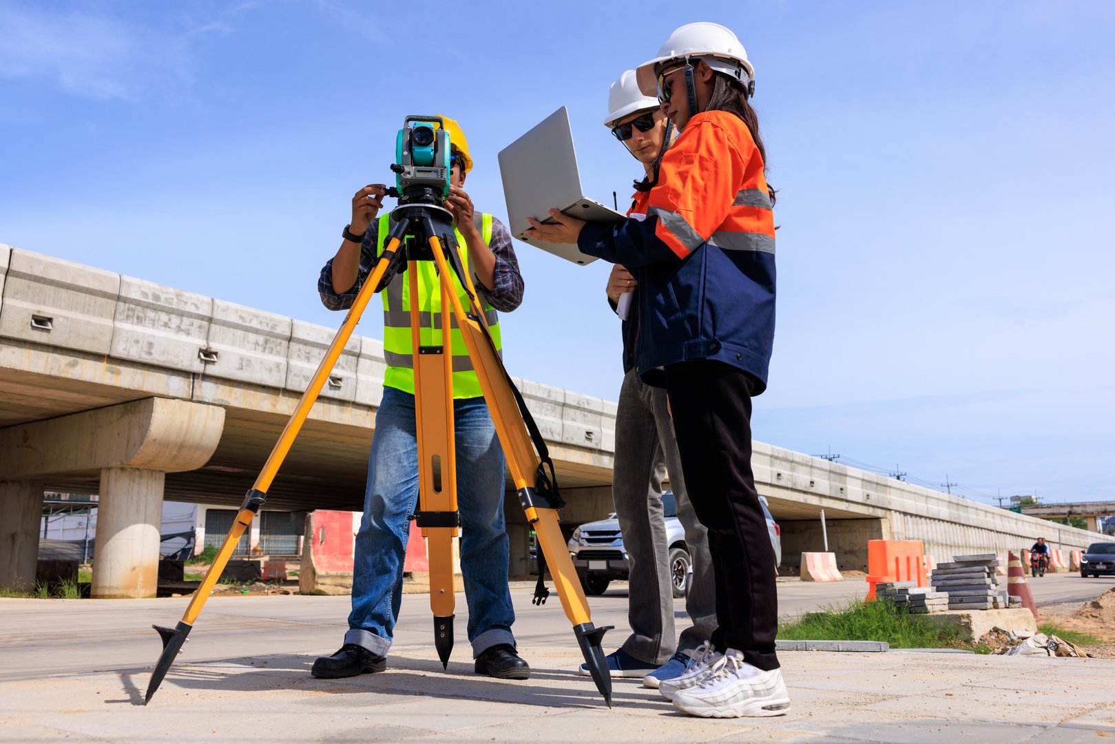 three engineer use theodolite equipment and looking blueprints  project on laptop for route surveying to build a bridge across the intersection to reduce traffic congestion during rush hours