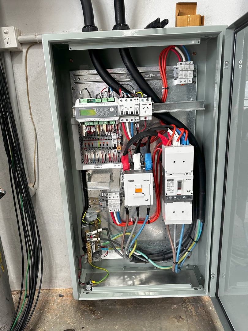 Open electrical control panel with wiring, circuit breakers, and a display screen in a metal casing.