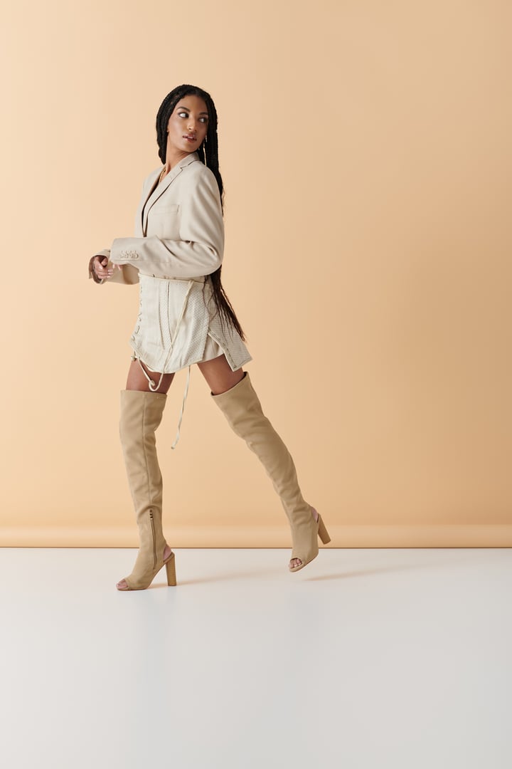 A young woman with braided hair showcases her fashionable outfit, exuding confidence in a bright studio.