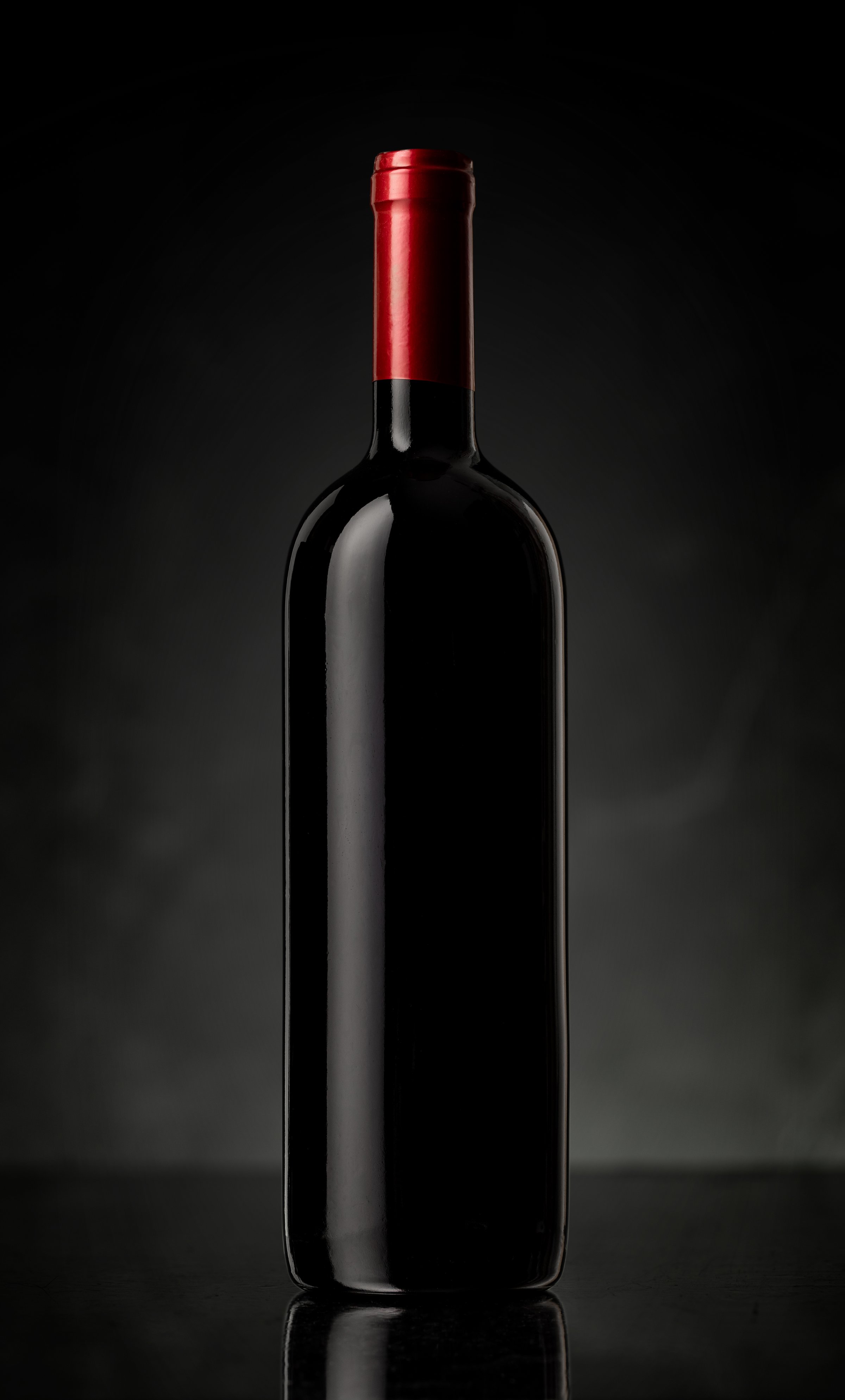 Unlabeled bottle of red wine on the dark glossy surface with reflection with stone background. Luxurious style.