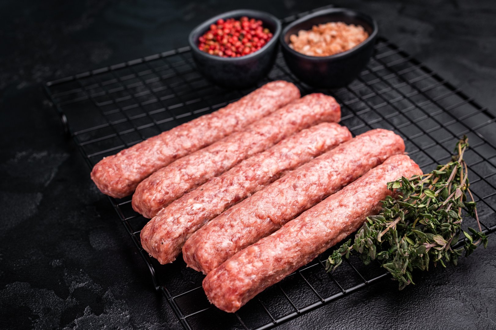 Uncooked Raw Cevapcici Sausage, fresh Cevapi from mince beef and pork meat on a rack. black background. top view.
