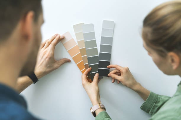 Two people selecting from paint swatches in neutral colors. Hands holding swatches on a white background.