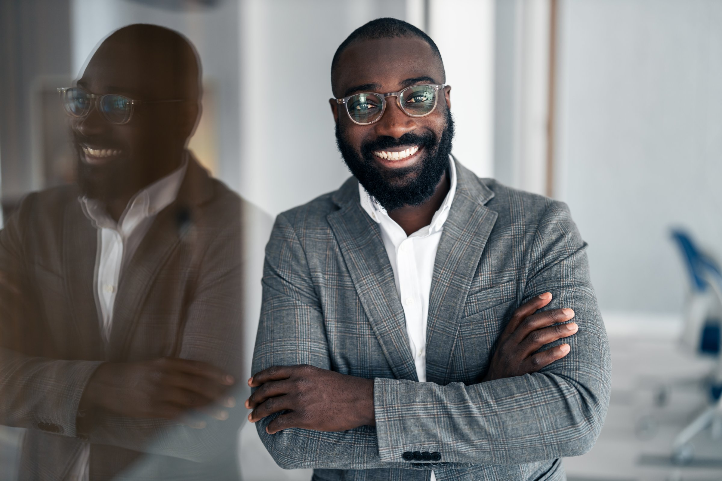 Confident Black businessman standing with arms crossed in a modern office