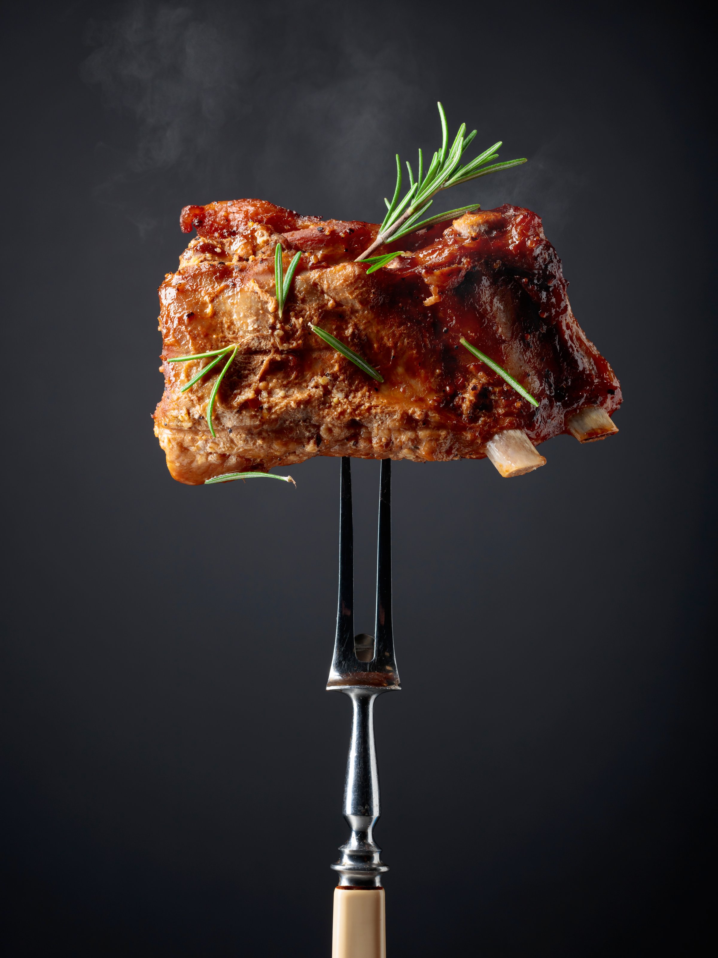 Grilled pork ribs on a fork. Grilled meat sprinkled with rosemary on a black background.