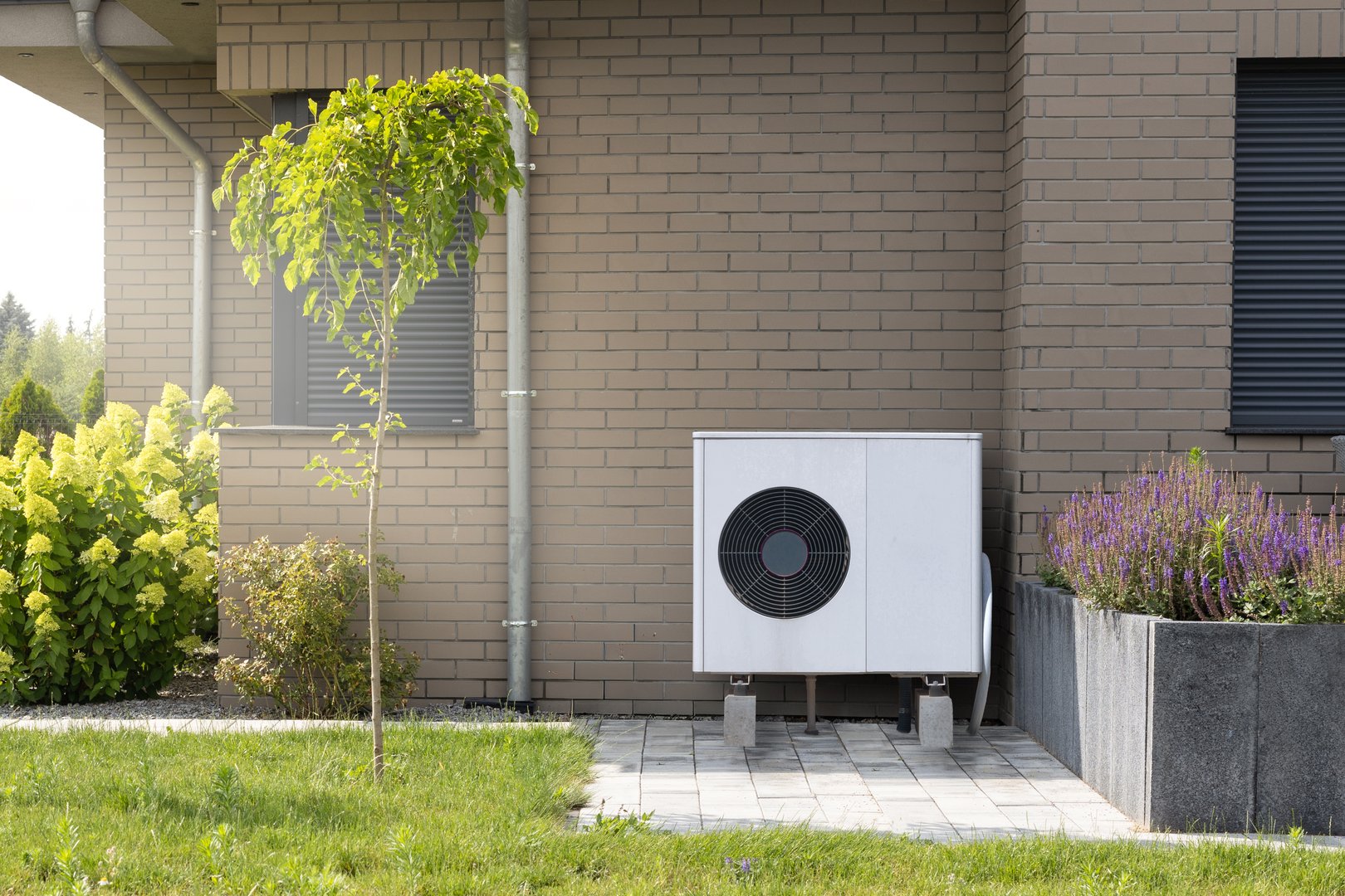 Modern heat pump system installed on the exterior of a building with plants and flowers.