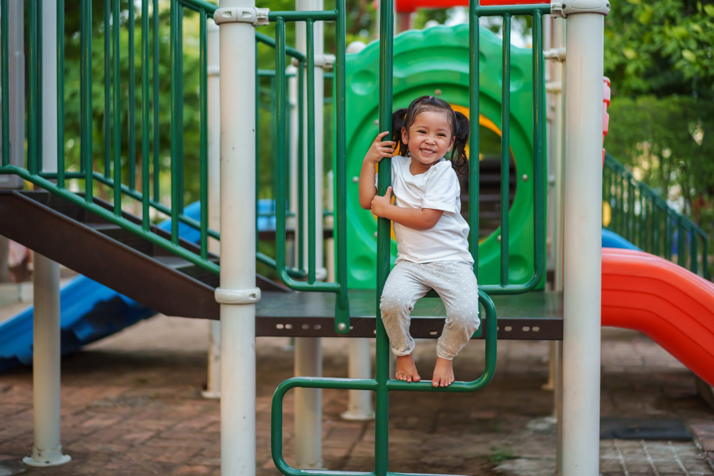 happy toddler girl playing and climbing on outdoor playground at the park