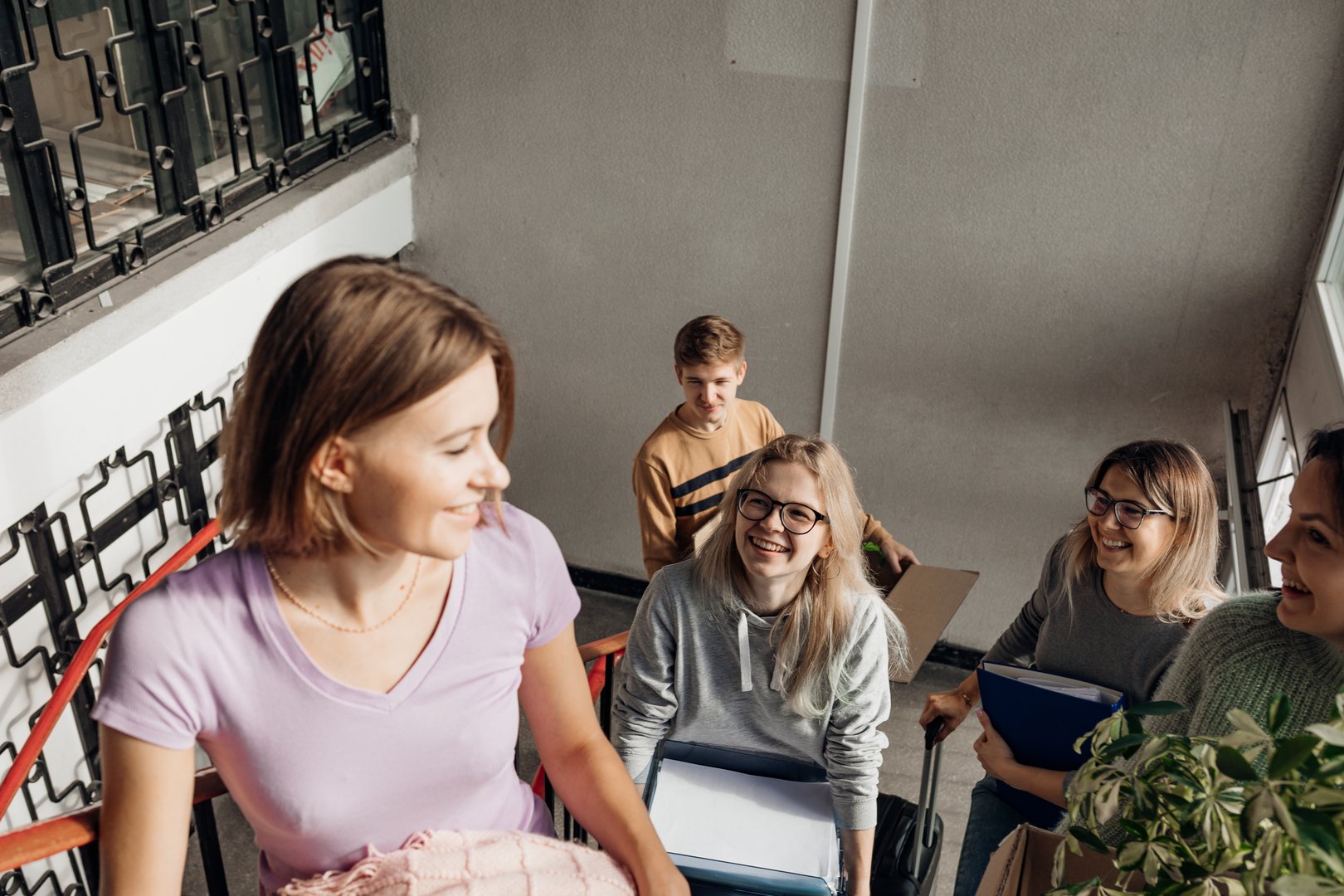 Smiling, glad, foretaste, anticipating students carrying luggage and stuff on the stairs, talking and joking while passage relocation. New friends, new neighborhood and roommate in college campus.