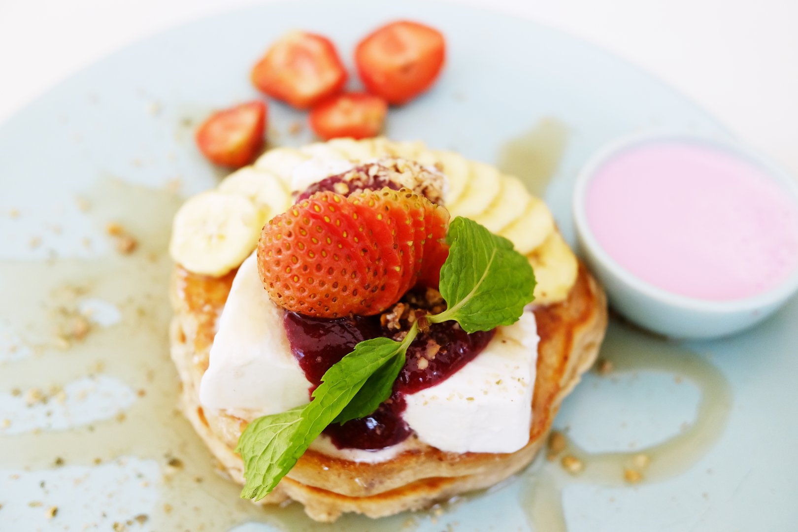 homemade pancake with fresh banana with strawberries and raspberry sauce, honey in whipped cream on white plate
