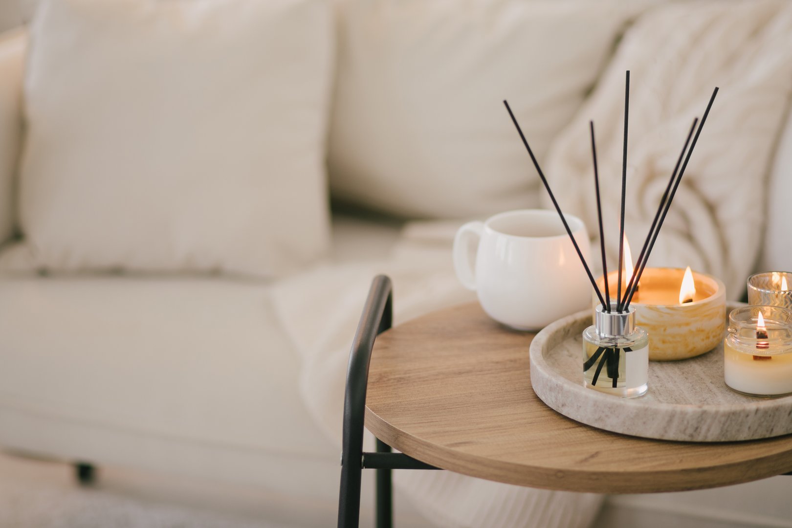 Still life with white mug, aromatic sticks and candles on a table in a cozy living room with white walls.