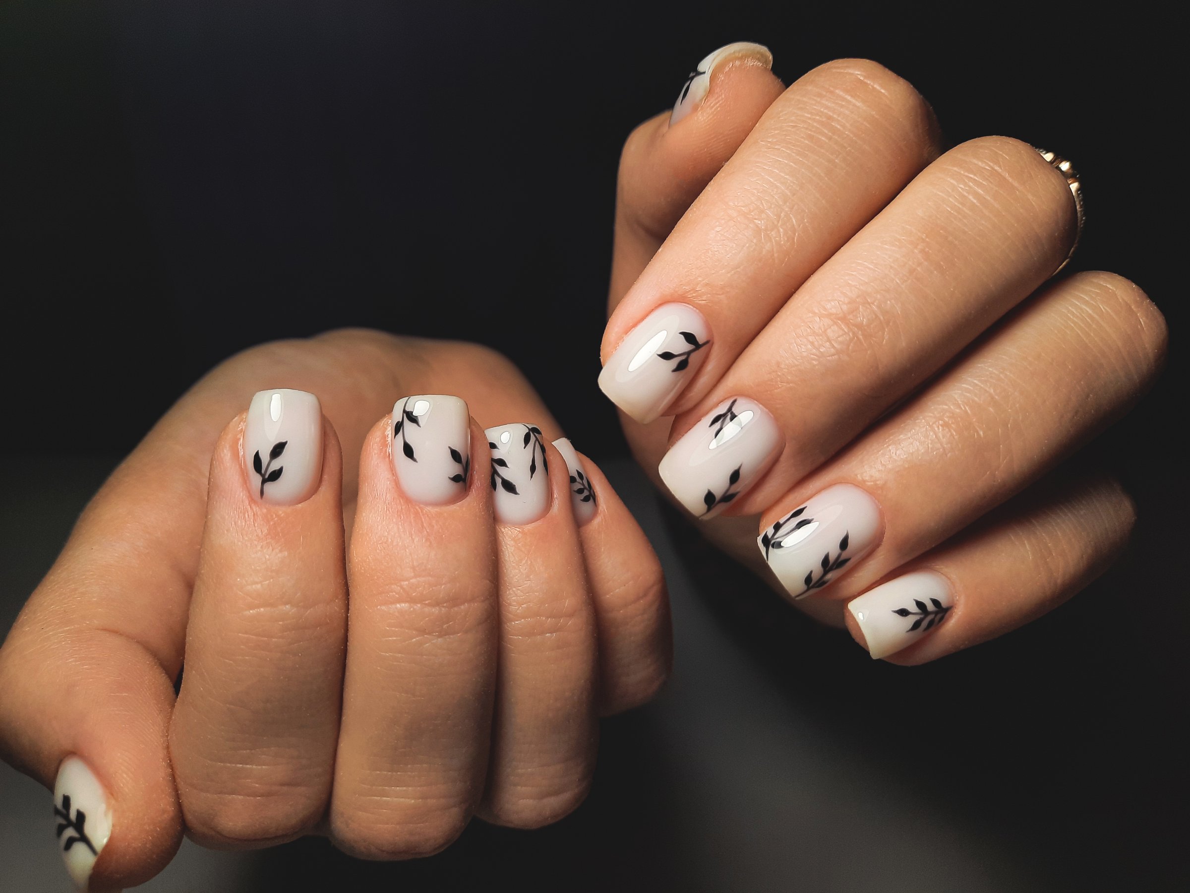 Women's manicure with a pale beige gel polish and twig design. Women's hands with a coating camouflage color on the nails and black branch design.