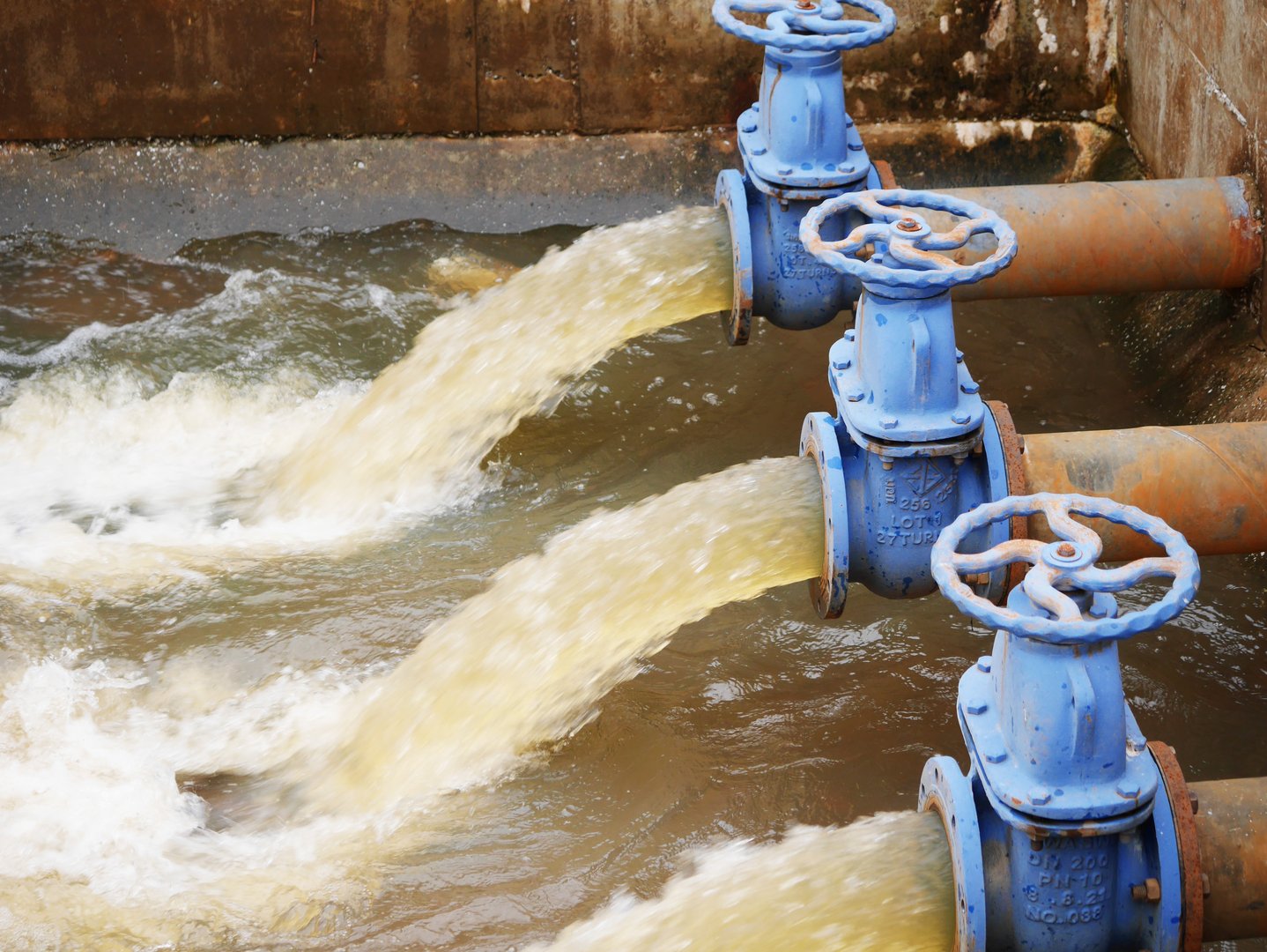 Industrial drainage system with five blue pipes discharging water into a reservoir. Concept of water management, wastewater treatment, and environmental engineering, spillway