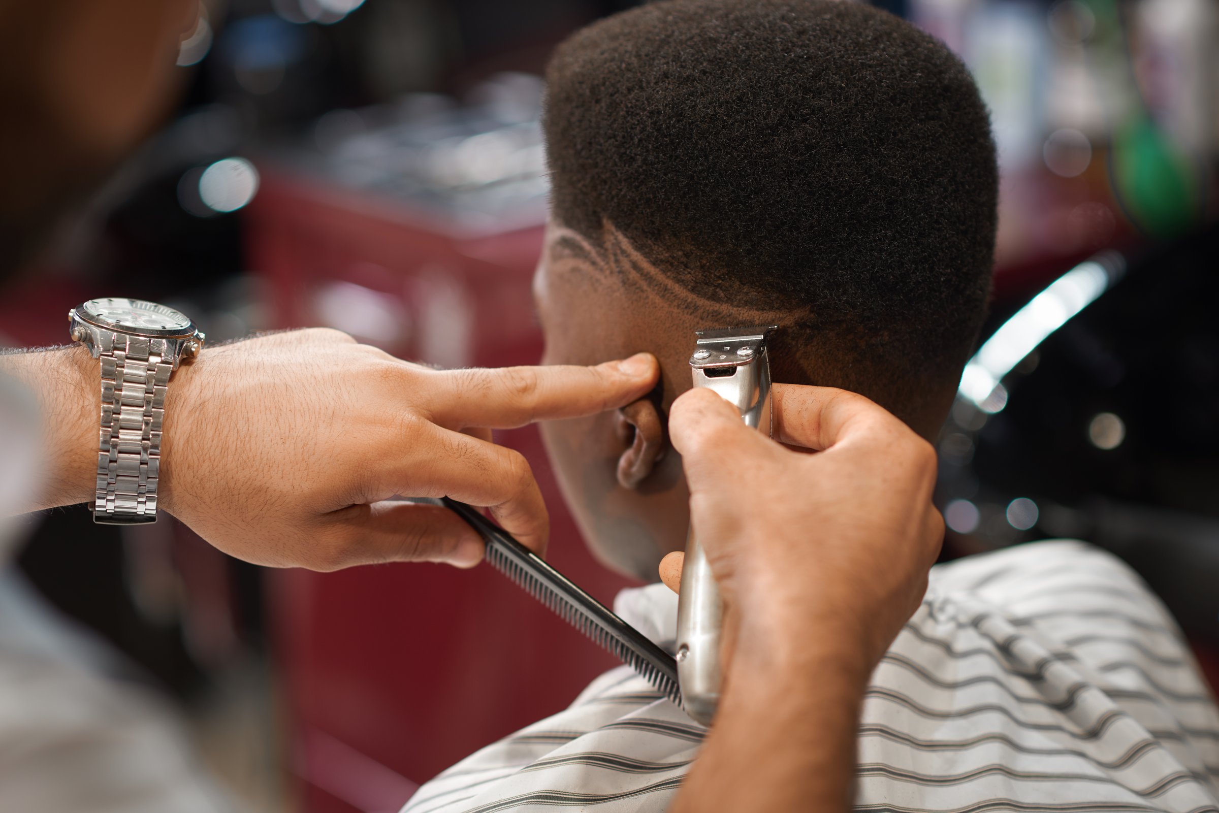 Closeup of process of trimming trendy stripes on head in barber shop. Barber keeping clipper and comb in hands and cutting hair to male sitting on chair. Concept of hairdressing and shaving.