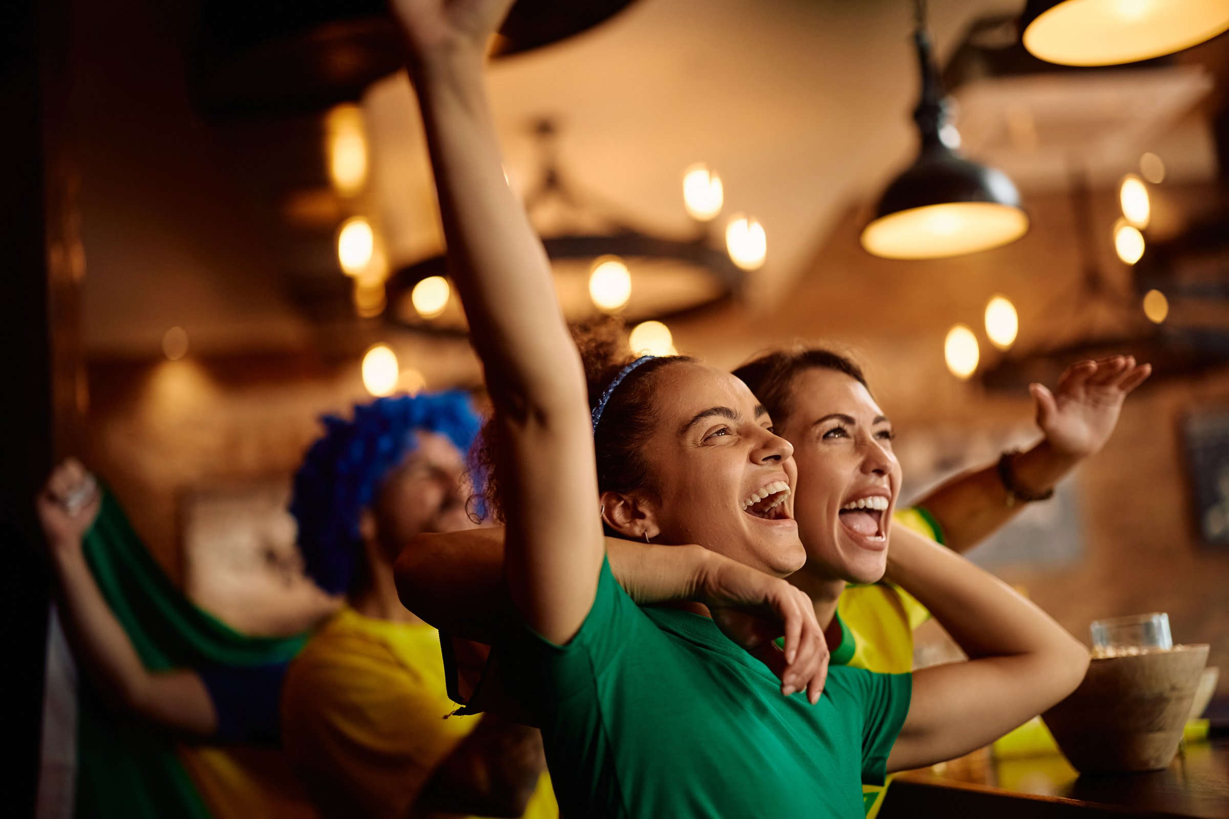Excited female fans watching sports match on mobile phone and celebrating after the winning goal of their favorite team.