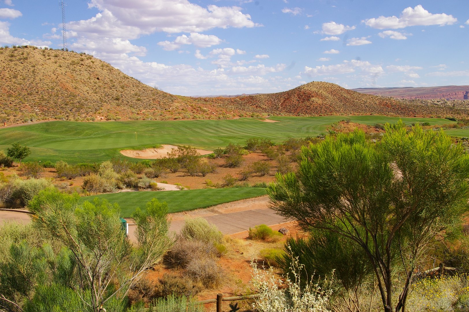 A scenic view from hilltop of golf course, mountains, and clear blue sky in Utah