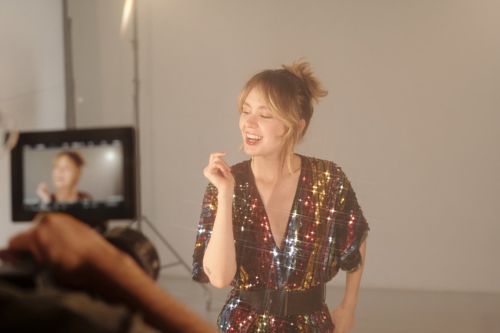 Waist up portrait of young woman smiling while performing in sparkly dress during music video shoot in studio