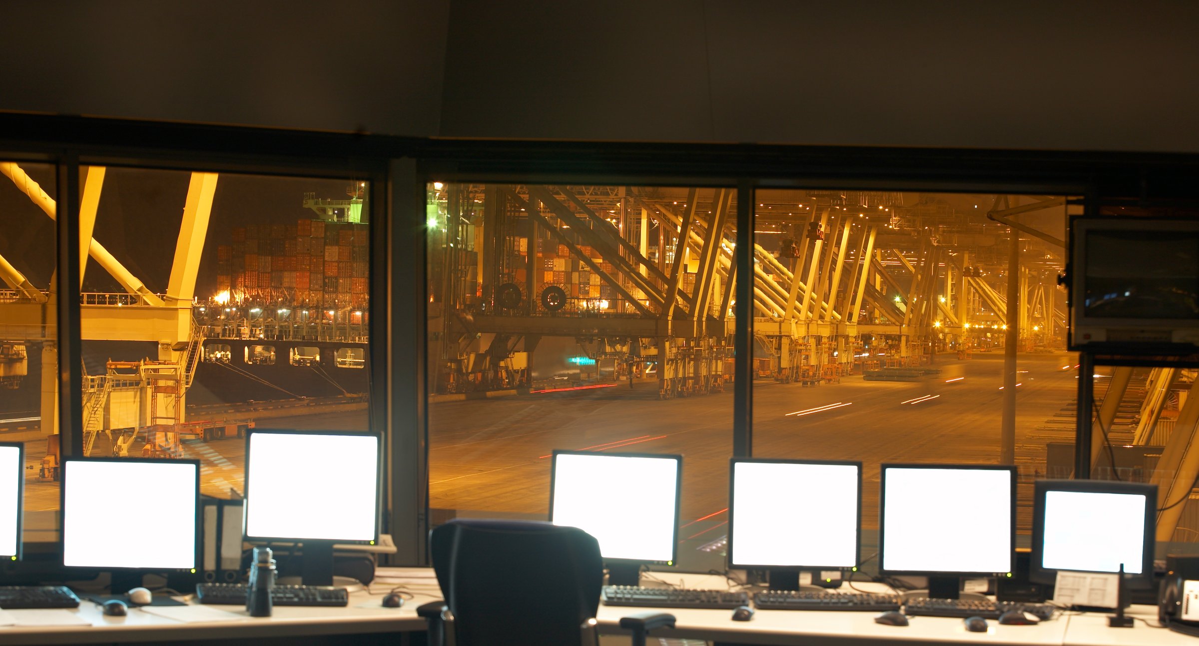 Control room in a harbor area at night, with cranes and ships in the background.