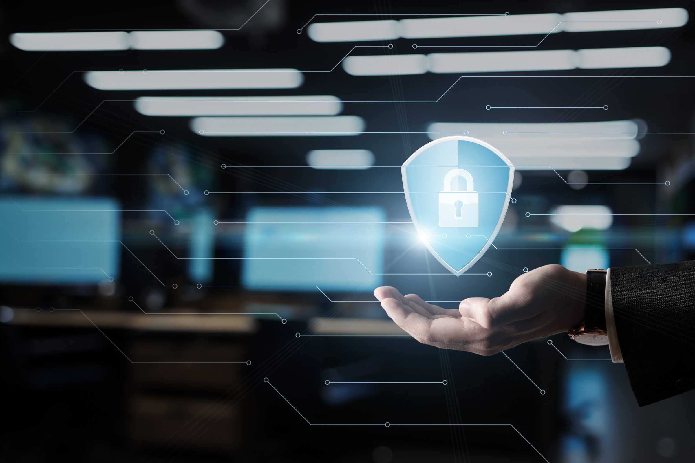 Protecting digital assets with innovative security measures. A person holds a glowing shield icon symbolizing digital security and protection in a modern workspace.